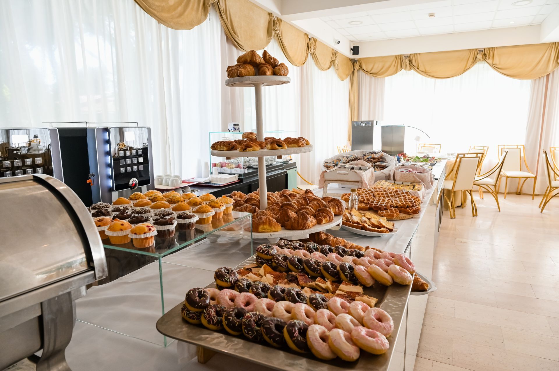 Tavolo del buffet di dolci con un assortimento di pasticcini e ciambelle in una luminosa sala per banchetti.