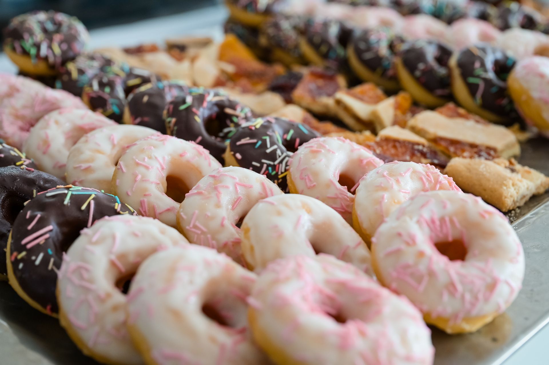 In una pasticceria, un assortimento di ciambelle ricoperte di cioccolato e glassate di rosa sono esposte su vassoi.