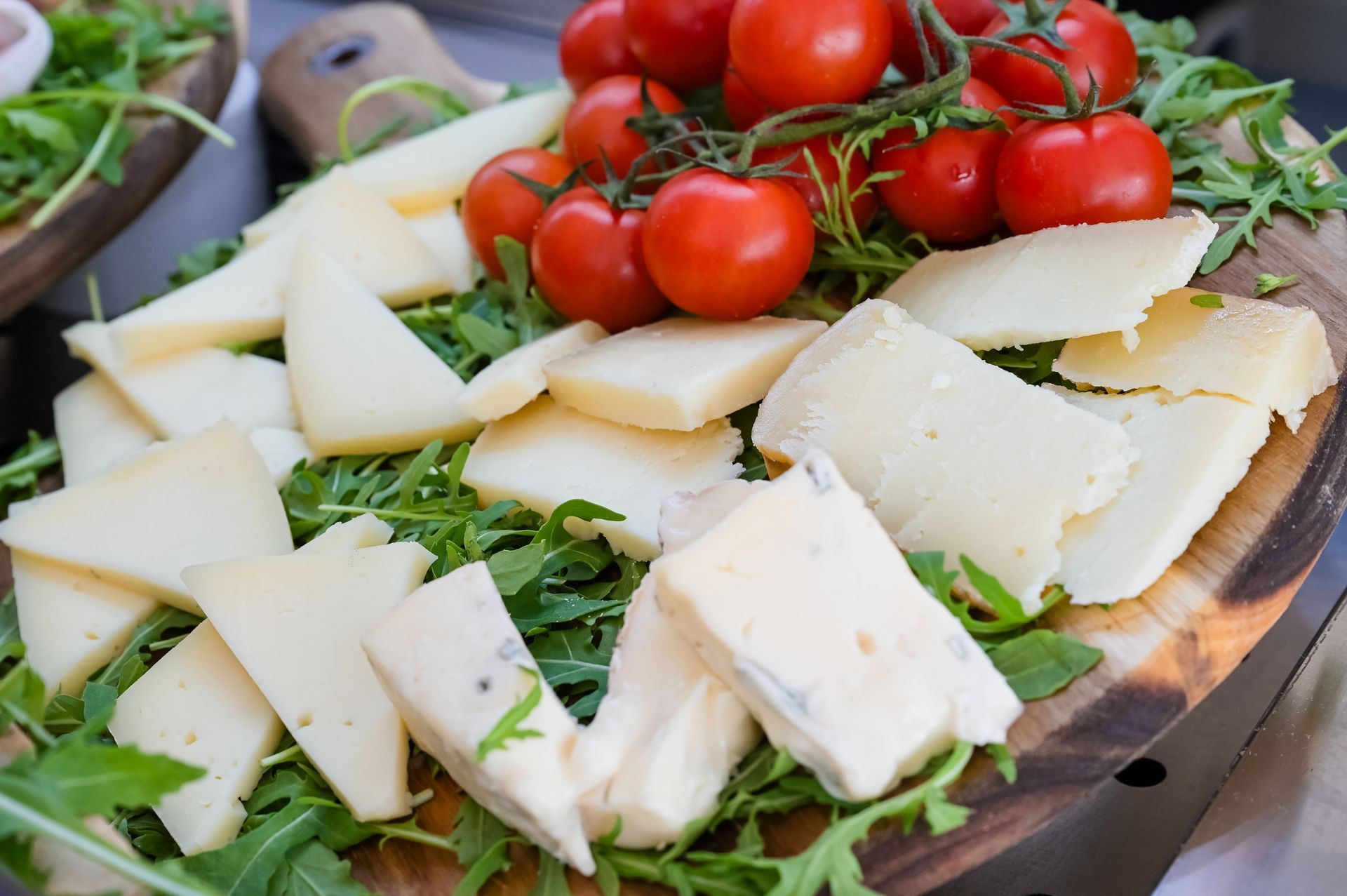 Formaggi assortiti, pomodorini e erbe aromatiche disposti su un tagliere di legno.