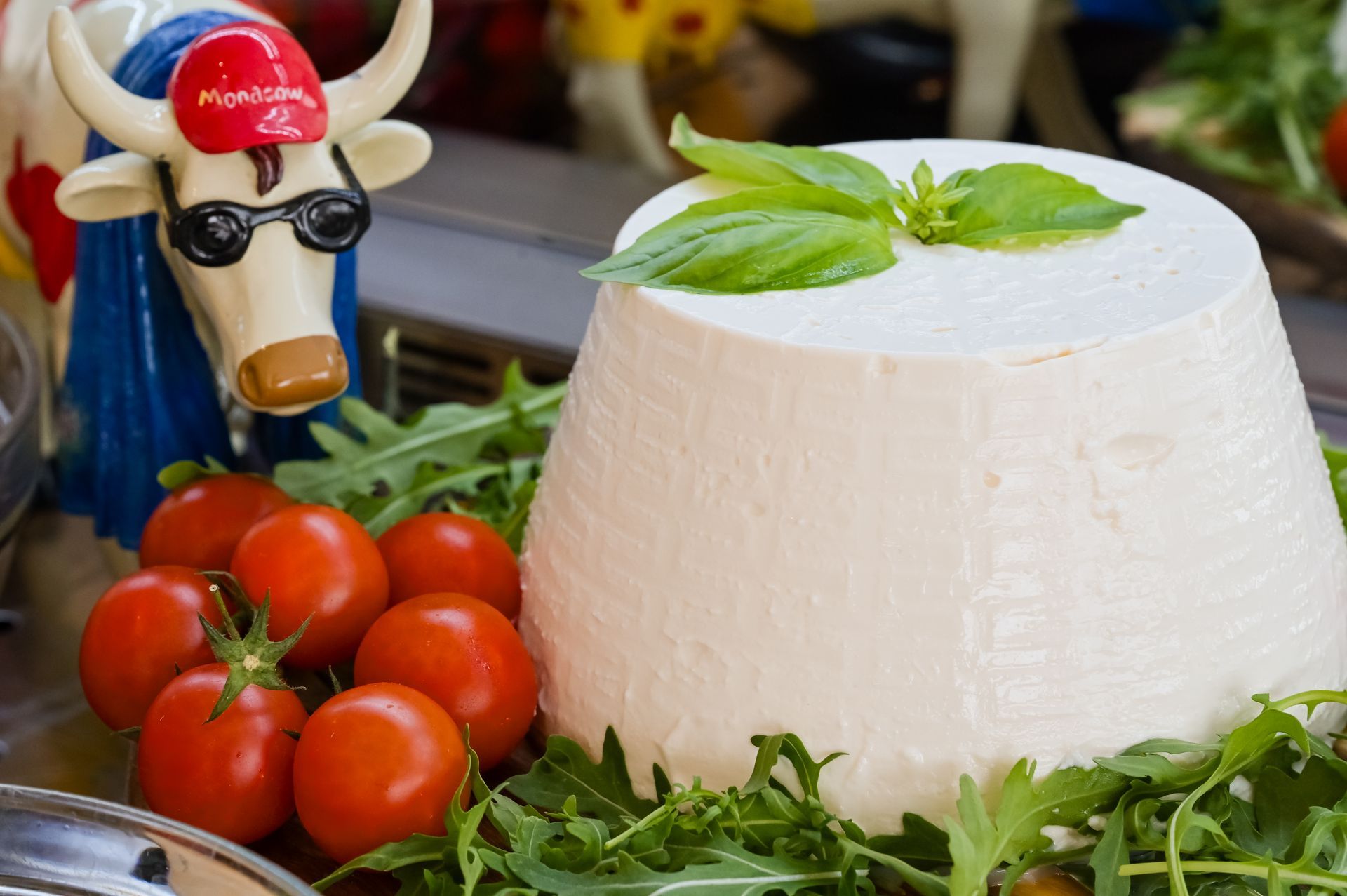 Cupola di formaggio bianco con basilico, pomodorini e una statuetta decorativa di mucca su un tavolo