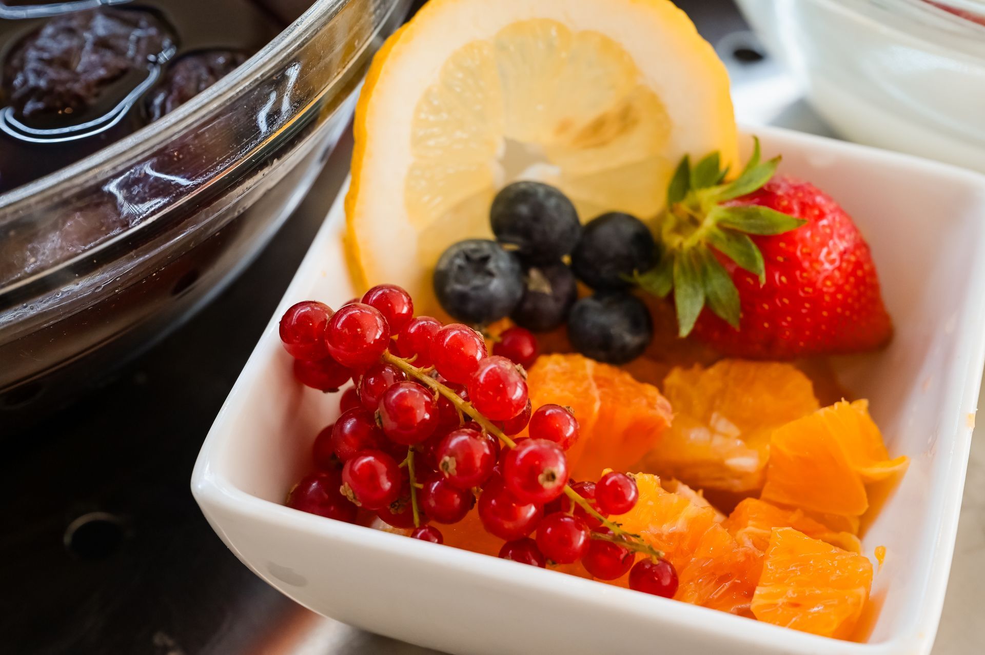 Una ciotola di frutta mista con fragole, mirtilli, ribes rosso, fette d'arancia e datteri su un tavolo.