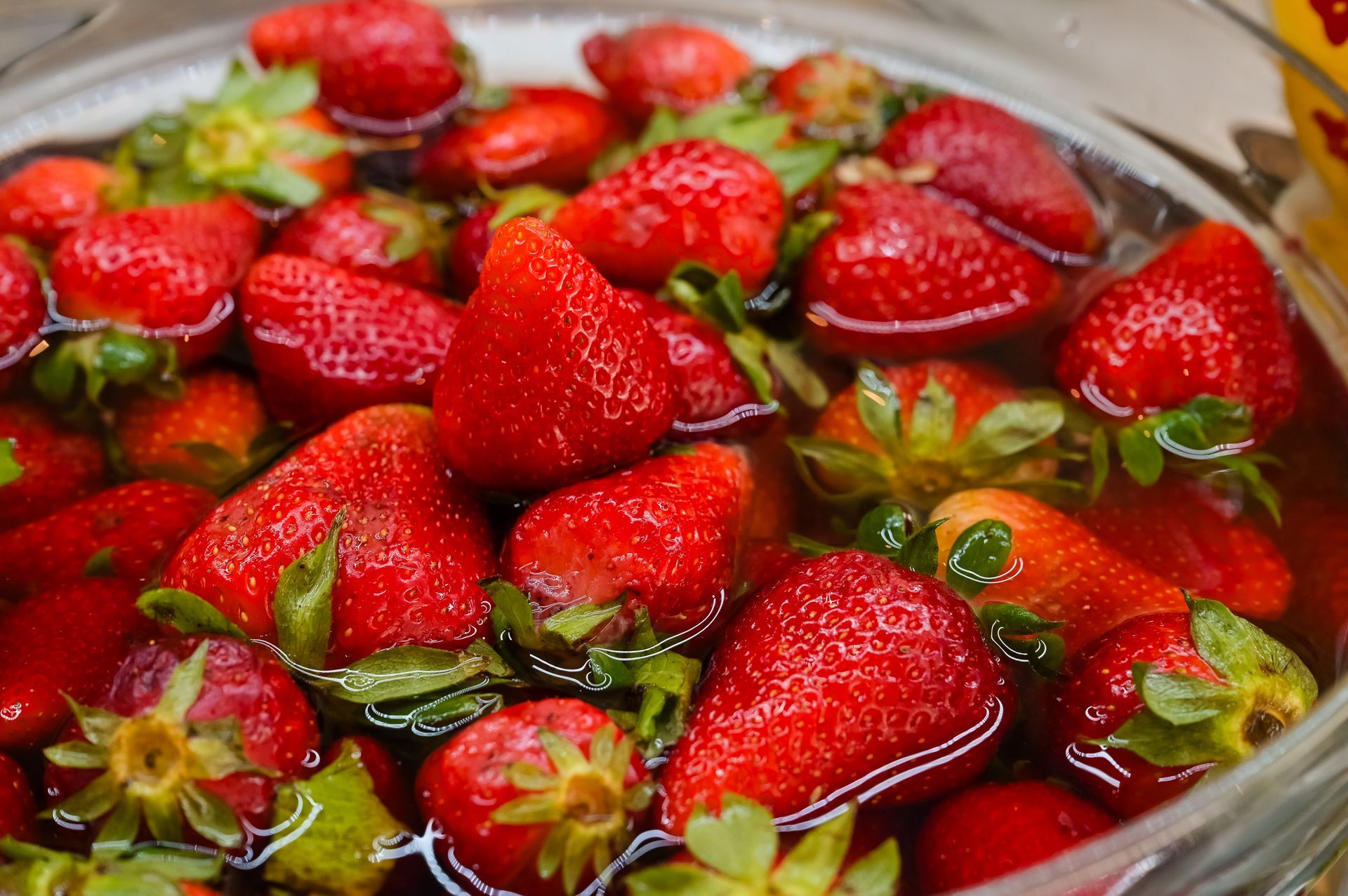 Una ciotola di fragole fresche immerse nell'acqua, con le fragole rosse e le foglie verdi ben visibili.
