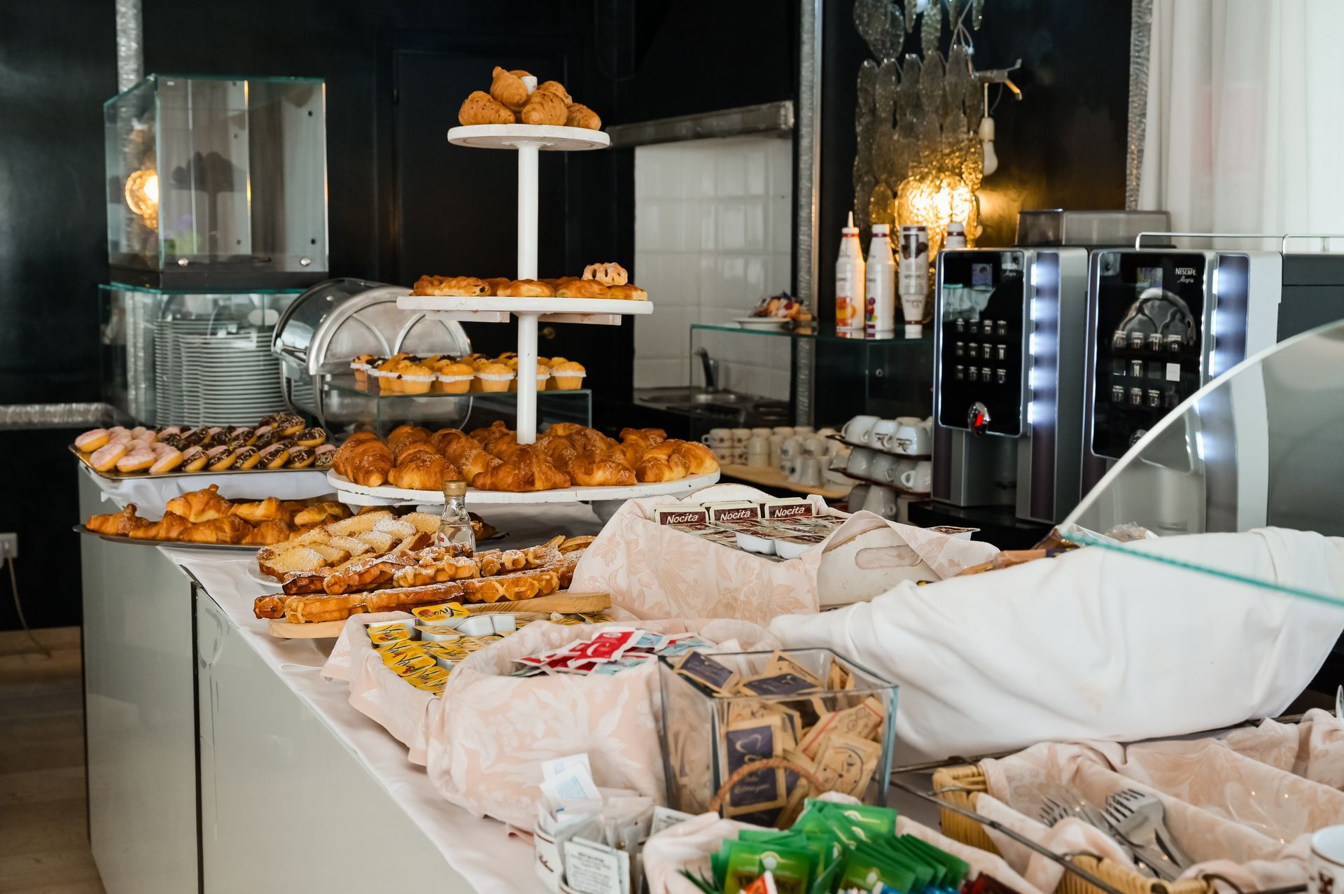 Tavolo da buffet con pasticcini e pane in una cucina o caffetteria luminosa.
