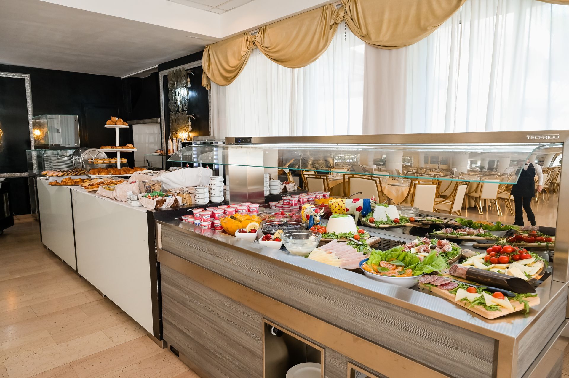Elegante tavolo da buffet con piatti assortiti, insalate e dessert in una sala banchetti con drappeggi dorati.