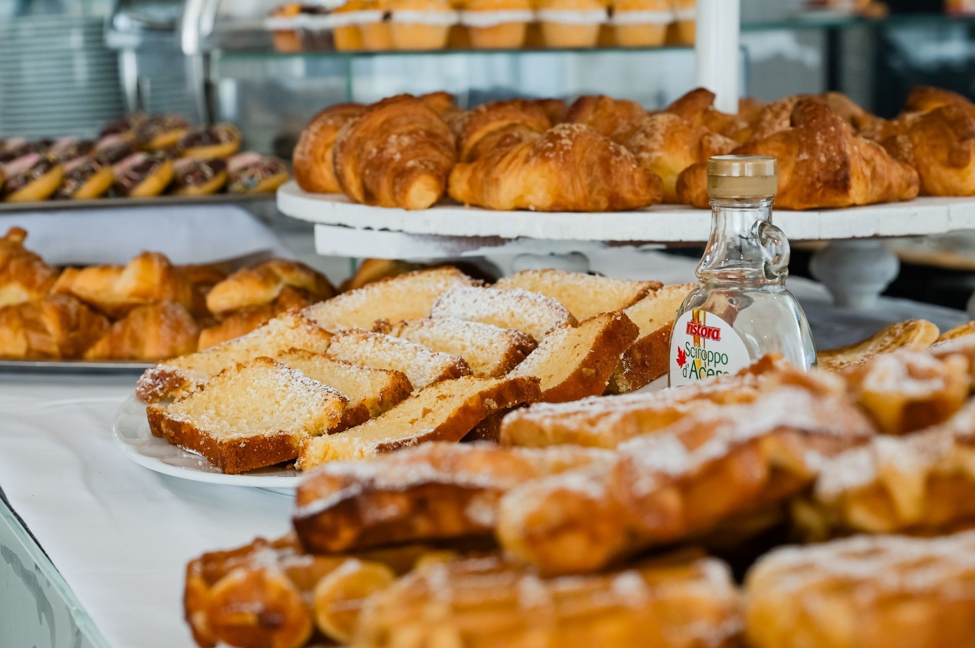 Assortimento di pasticcini e pane a fette su vassoi in un buffet di panetteria con una piccola bottiglia di sciroppo