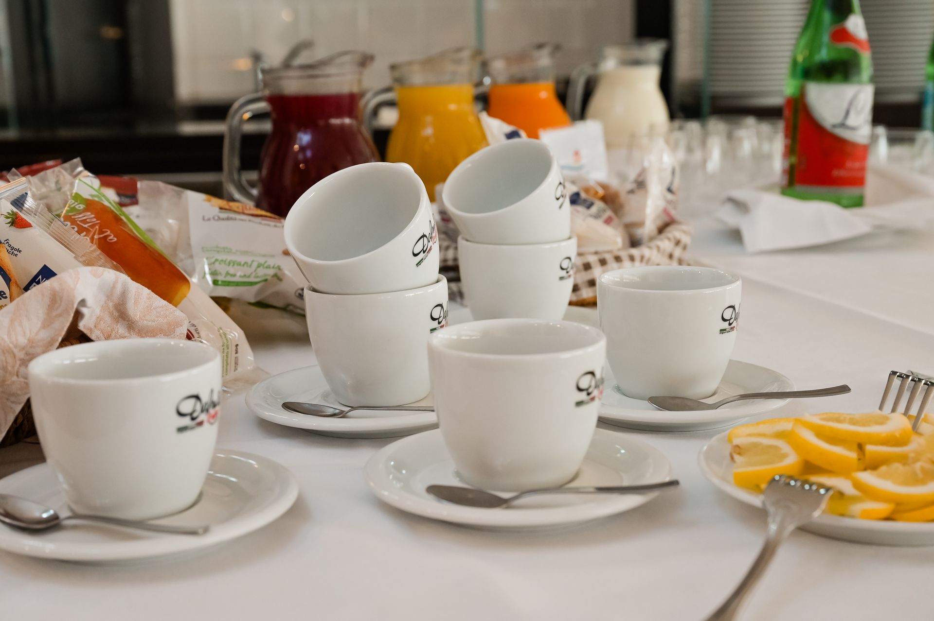 Tazzine da caffè bianche su piattini con pasticcini e frutta su un tavolo da colazione
