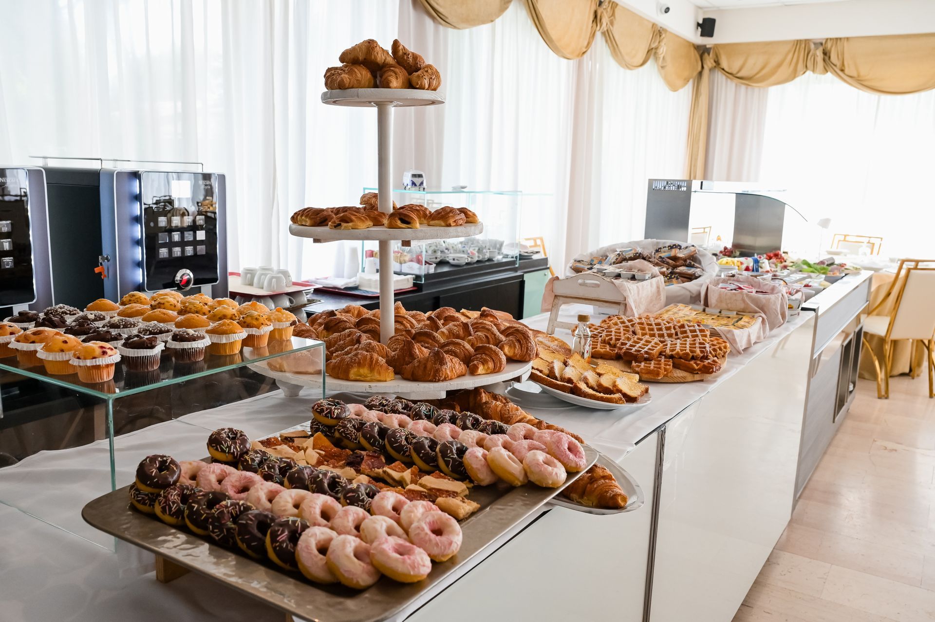 Un tavolo da buffet imbandito con un assortimento di pasticcini e ciambelle in una luminosa sala eventi.