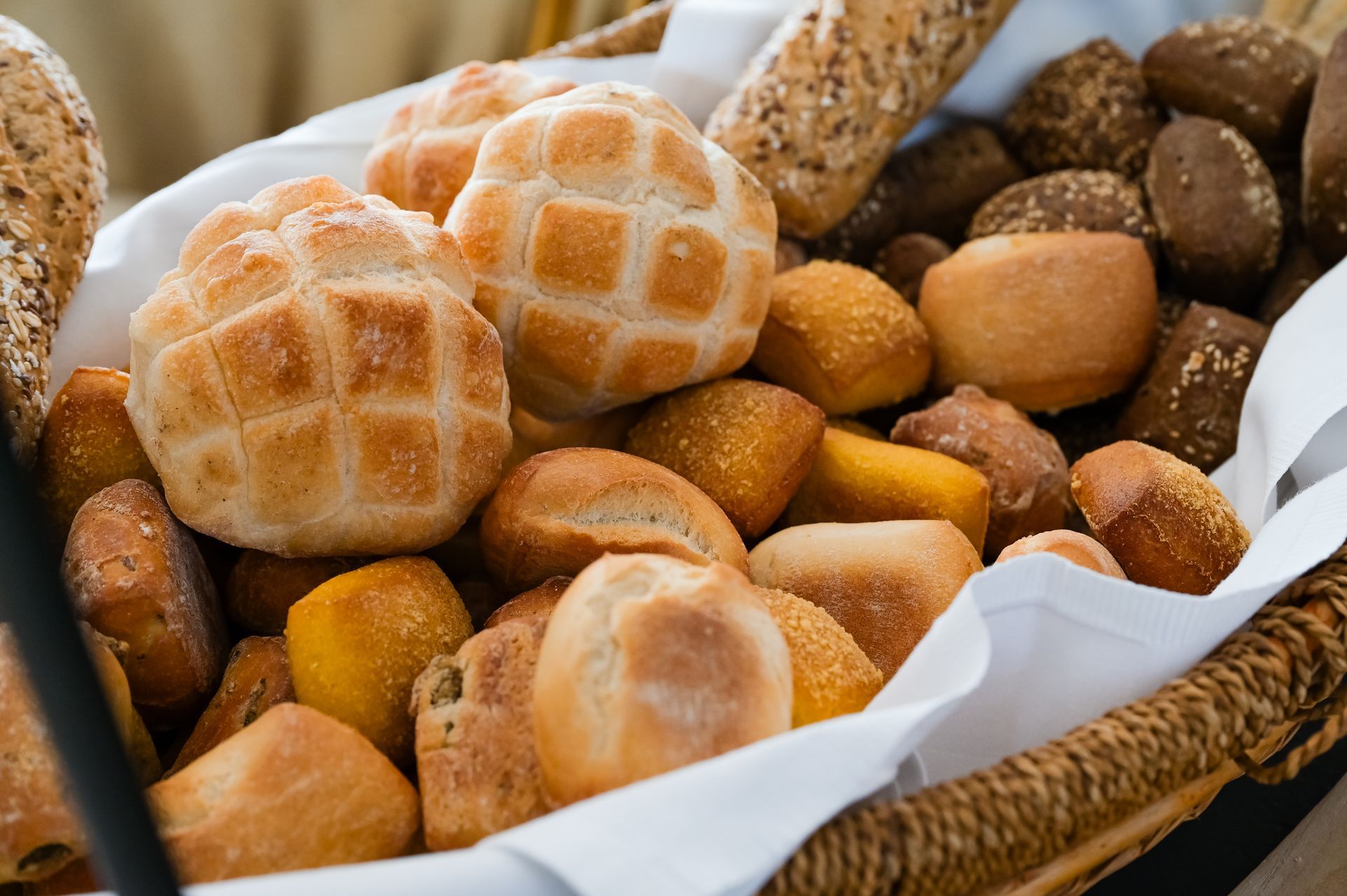 Cesto di panini e focaccine assortiti, tra cui due pagnotte incise, in un cesto di vimini foderato di bianco.