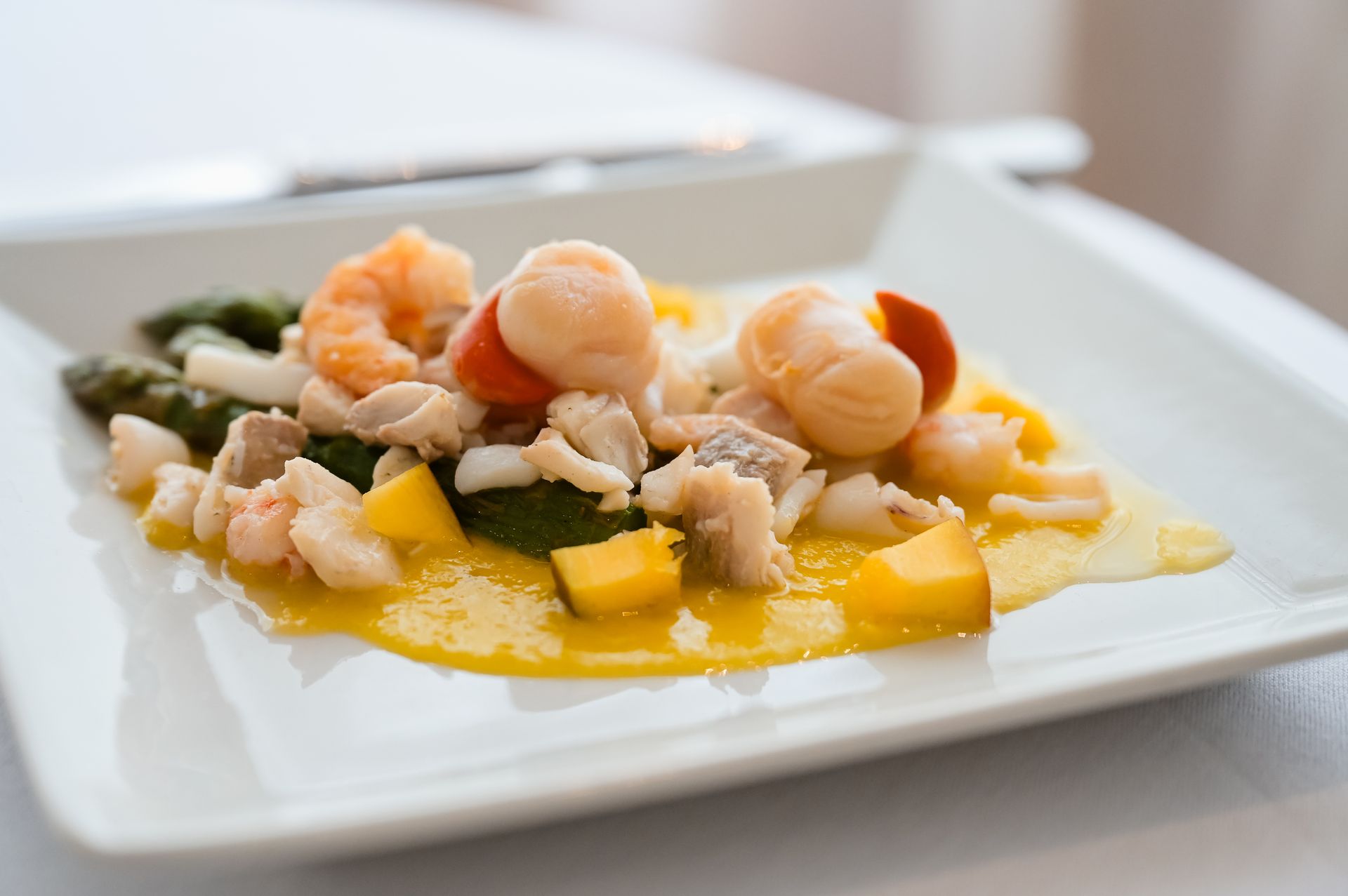 Gamberi e verdure serviti su un piatto quadrato bianco, guarniti con salsa.