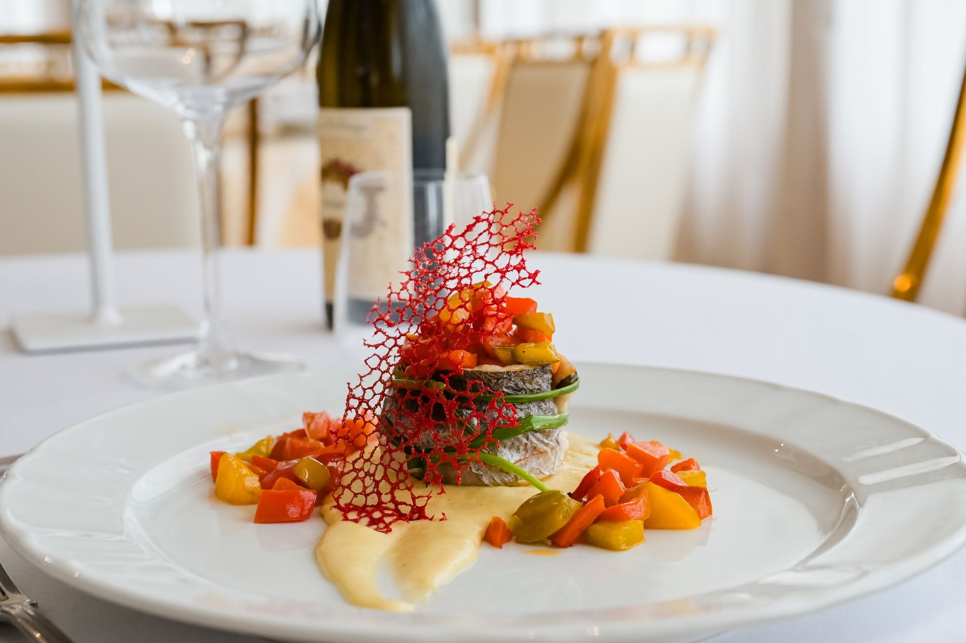 Antipasto gourmet servito su un tavolo bianco da ristorante, con verdure colorate tagliate a dadini e una guarnizione croccante di colore rosso.