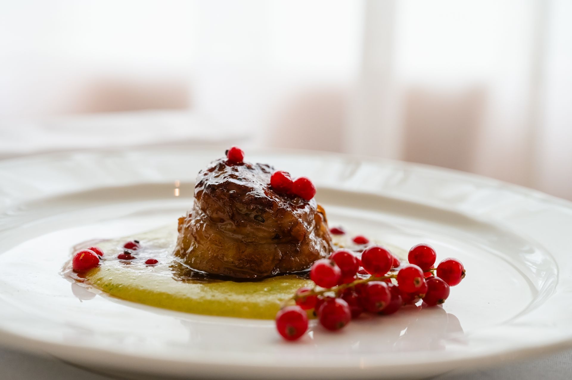 Dessert su un piatto bianco con frutti rossi e salsa, su una tavola apparecchiata in modo luminoso.