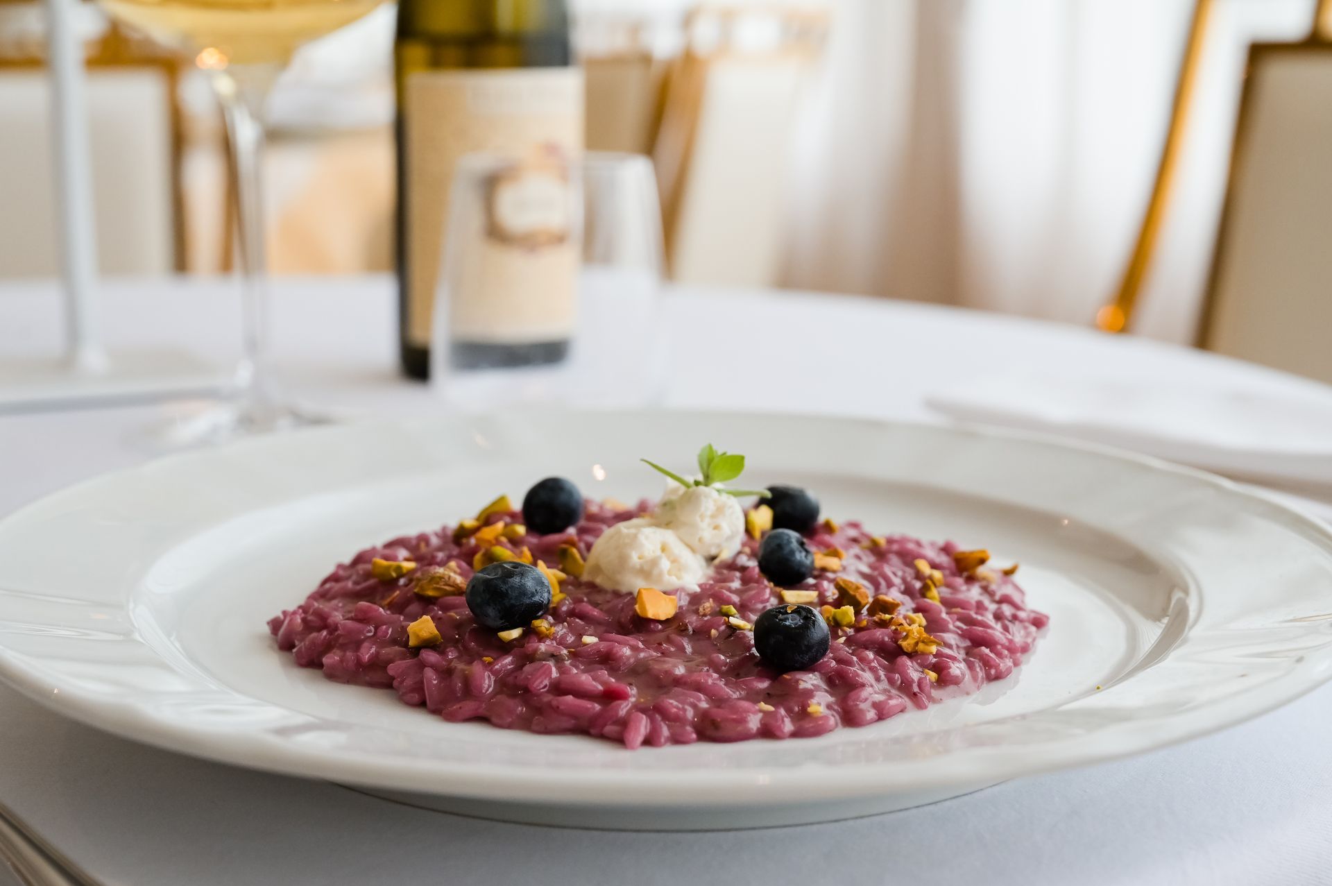 Risotto di barbabietola guarnito con frutti di bosco e formaggio su una tovaglia bianca in una sala da pranzo formale.