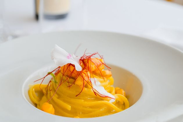 Pasta gialla allo zafferano guarnita con erbe aromatiche su un piatto bianco.
