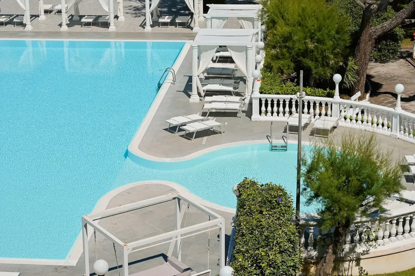 Piscina del resort con lettini bianchi, gazebo e acque turchesi sinuose.