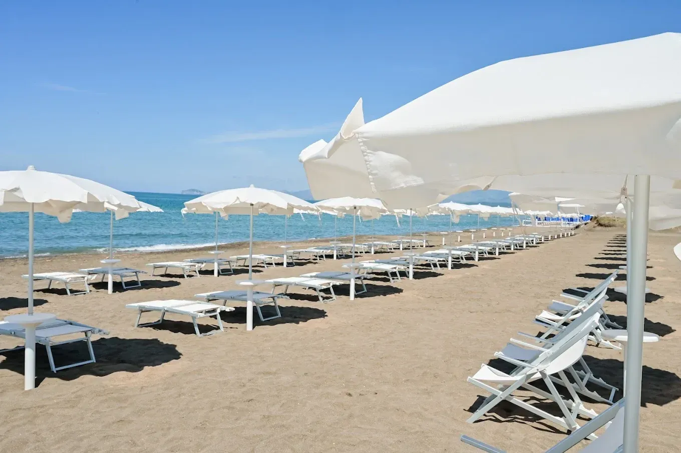 Spiaggia soleggiata con file di lettini bianchi e ombrelloni lungo la riva.