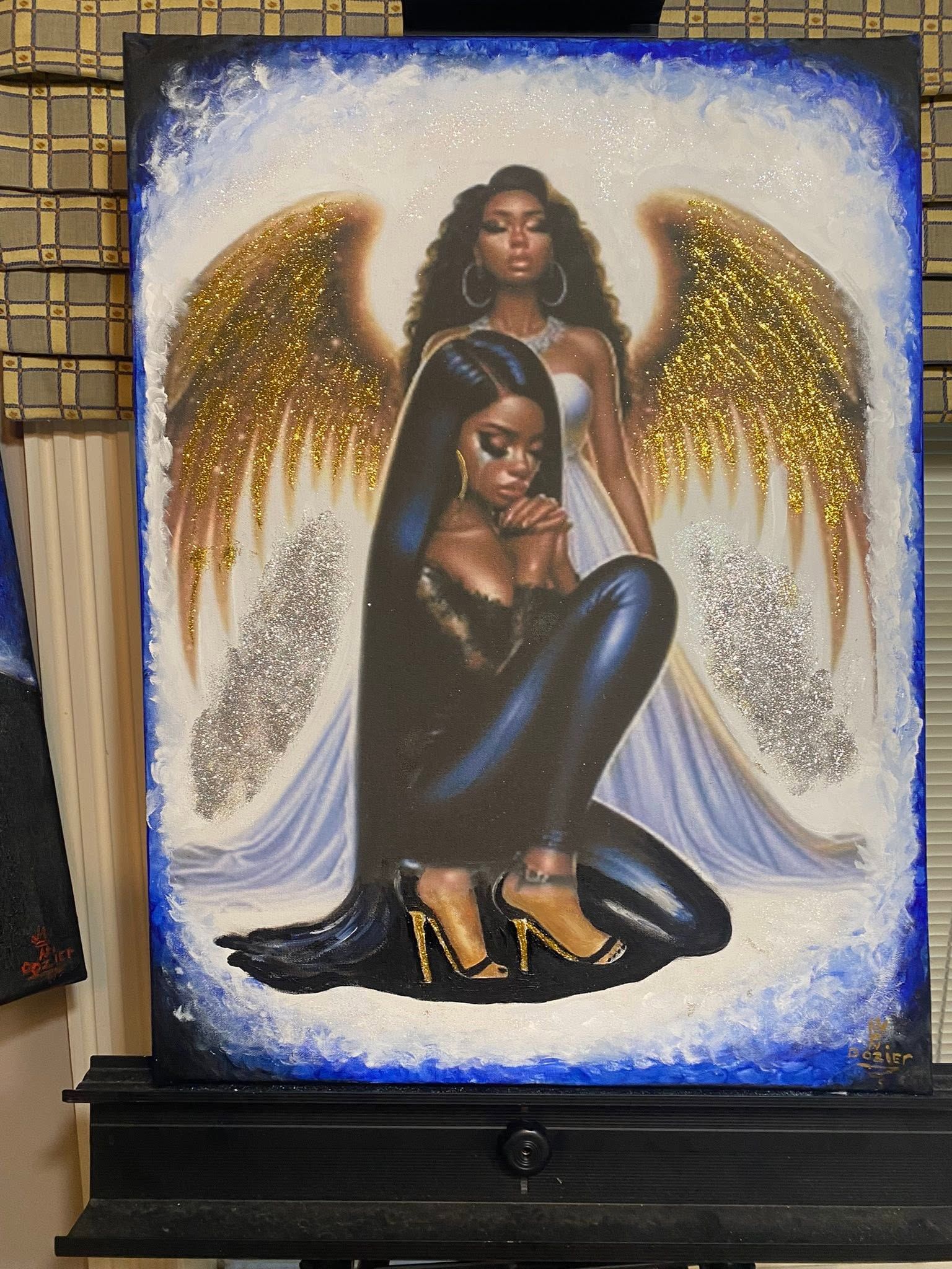 Fashion artwork of a seated figure in black with gold angel wings on a blue-bordered canvas