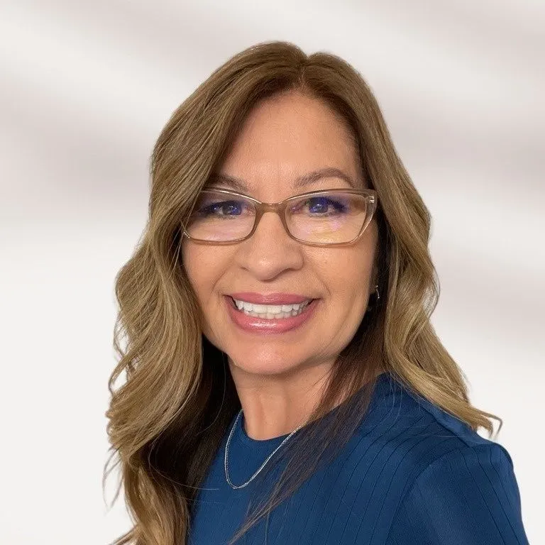 Smiling woman with two-toned dark and blonde hair wearing a grey blazer against a neutral backdrop.