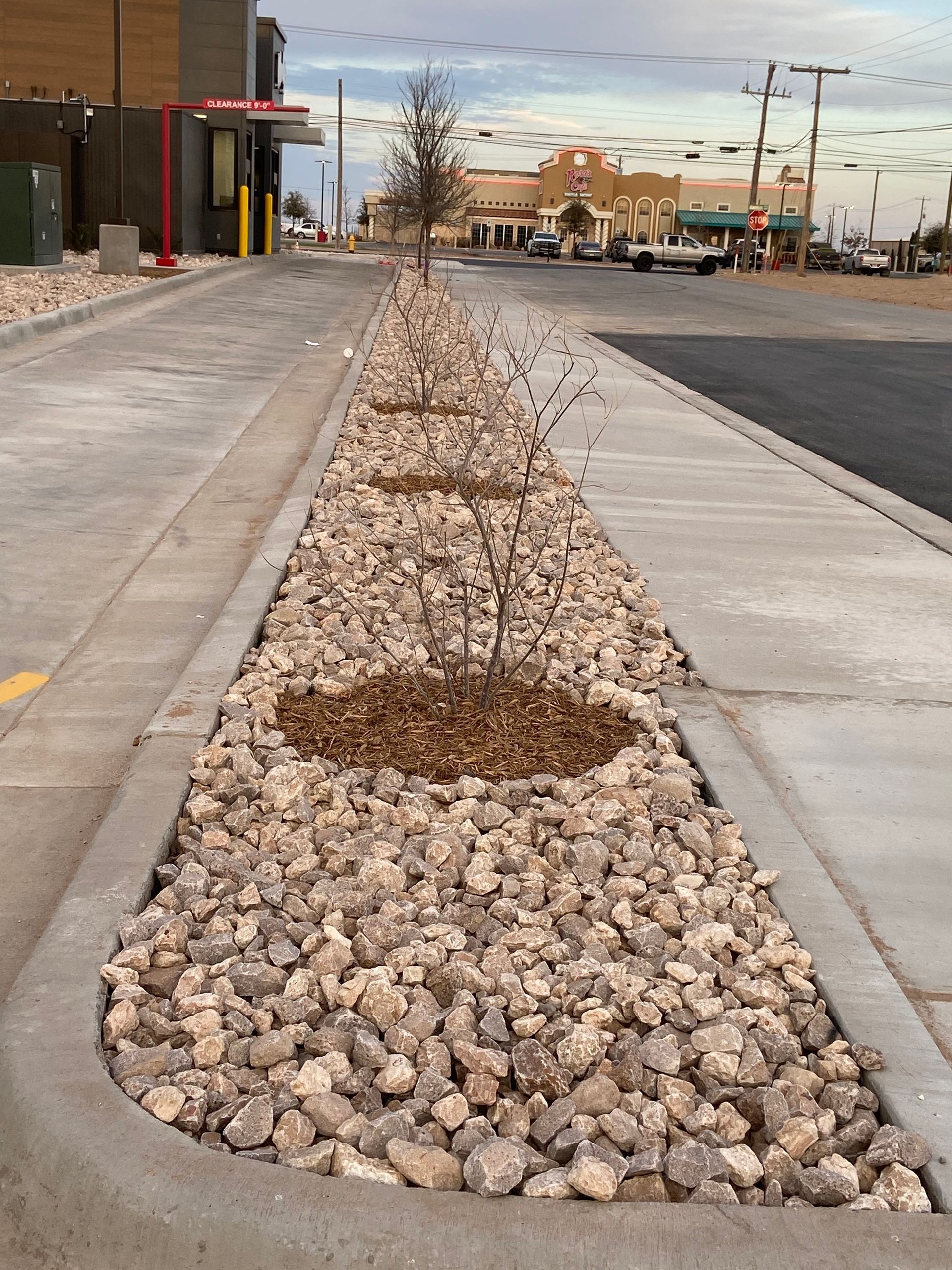 Rock-filled median strip along a sidewalk and road in a commercial area