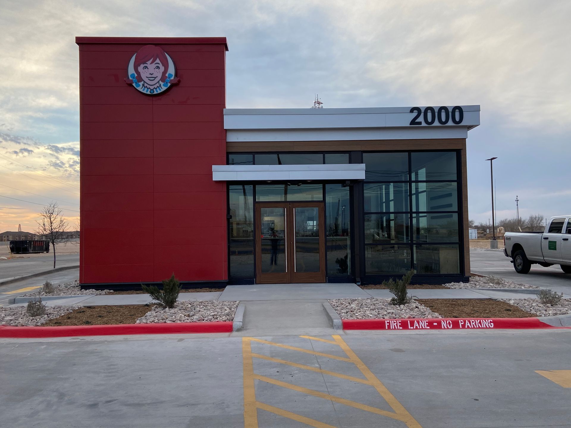 Red-and-glass storefront with number 2000 at the entrance and a parked truck nearby.