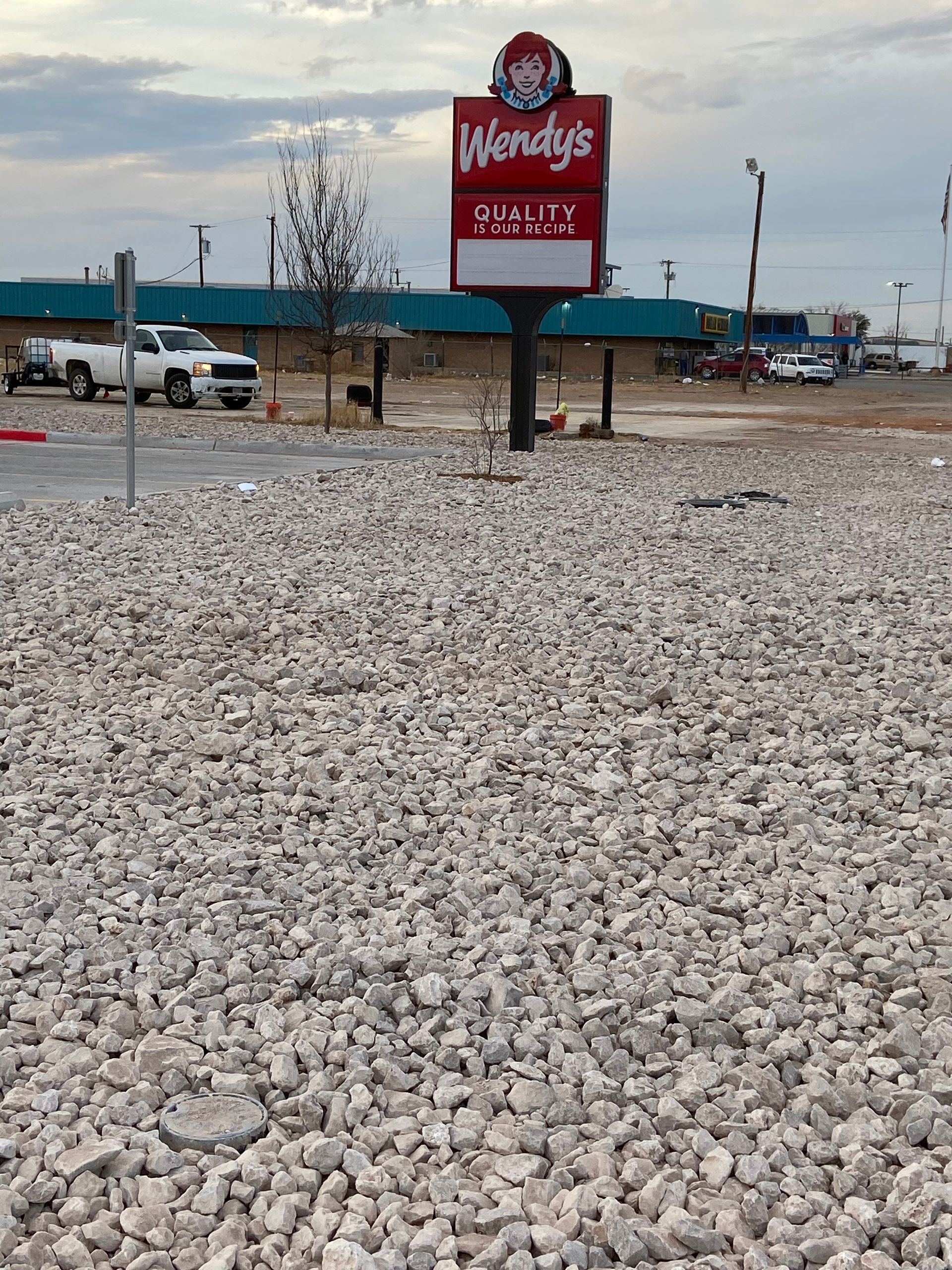 Gravel lot with a red Wendy’s sign and buildings in the distance under a cloudy sky.