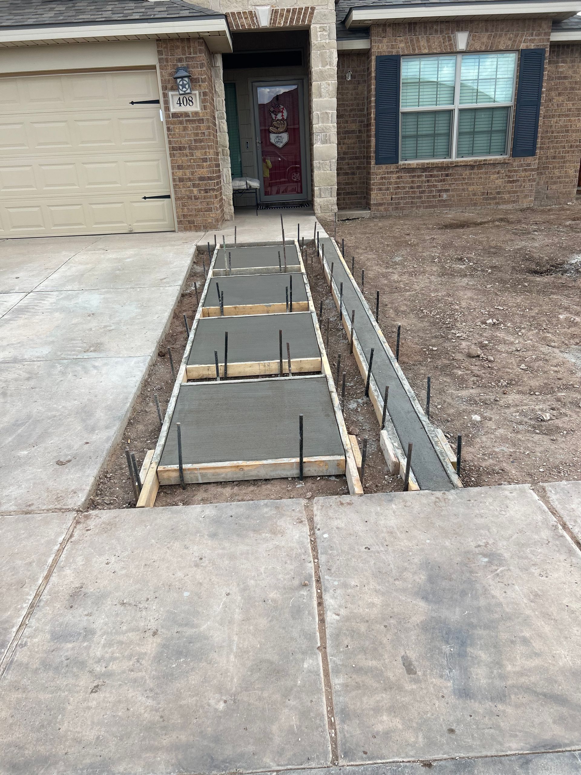 Damaged sidewalk ramp with exposed wooden forms leading to a house front door