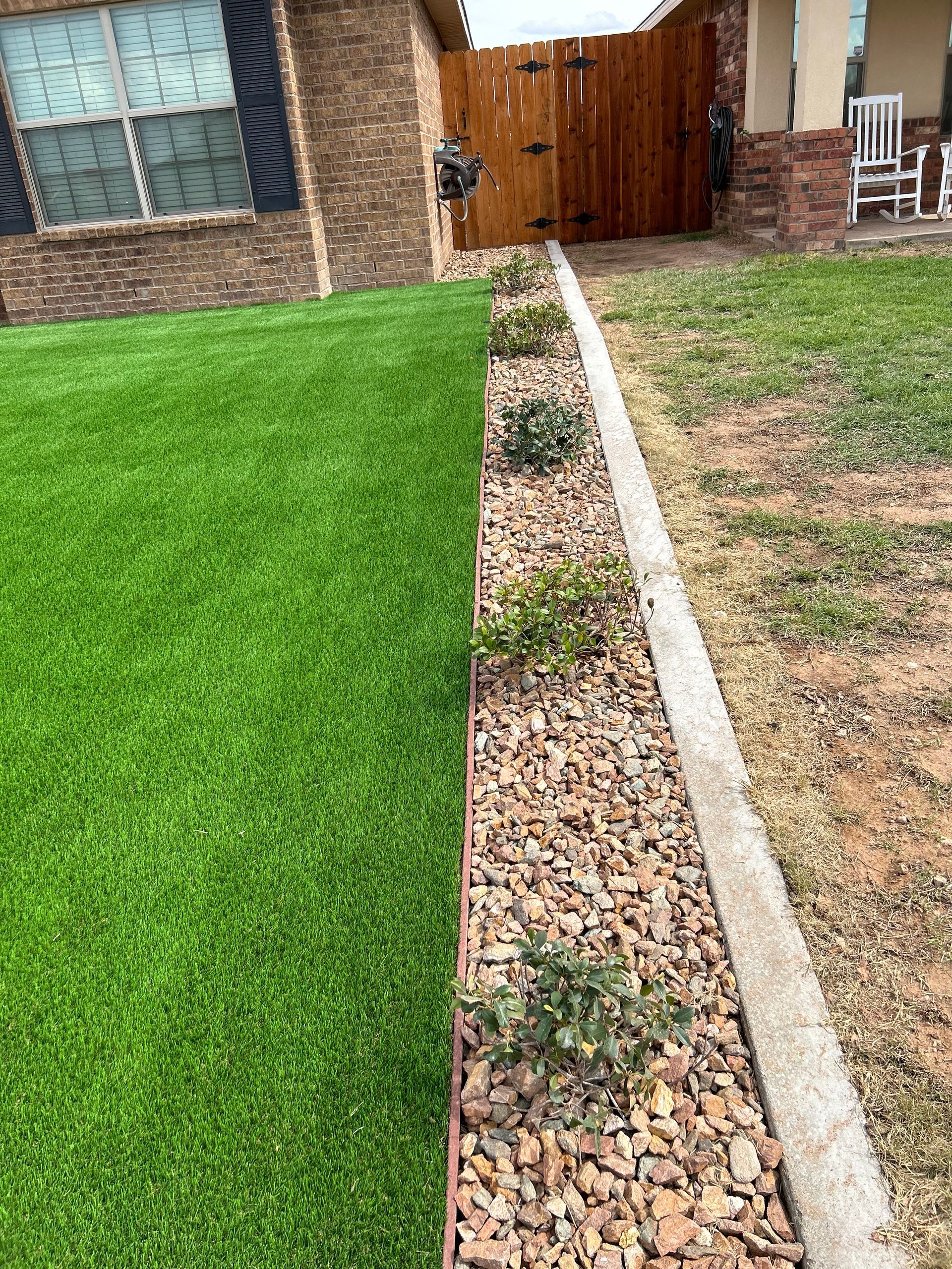 Backyard lawn edge with concrete border, gravel strip, and wooden gate near a brick house