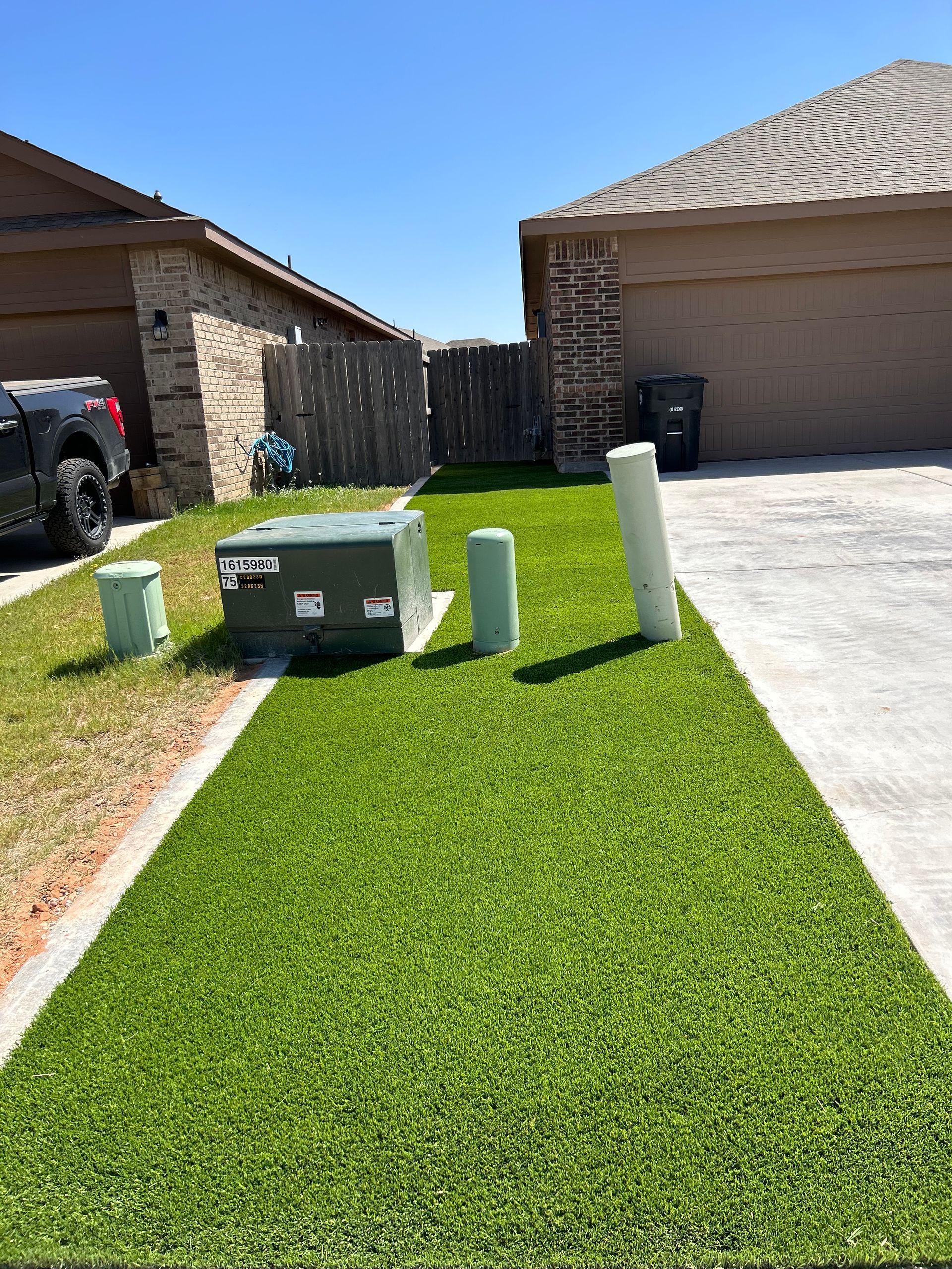Suburban front yard with green utility boxes and white pipes beside a driveway and house.
