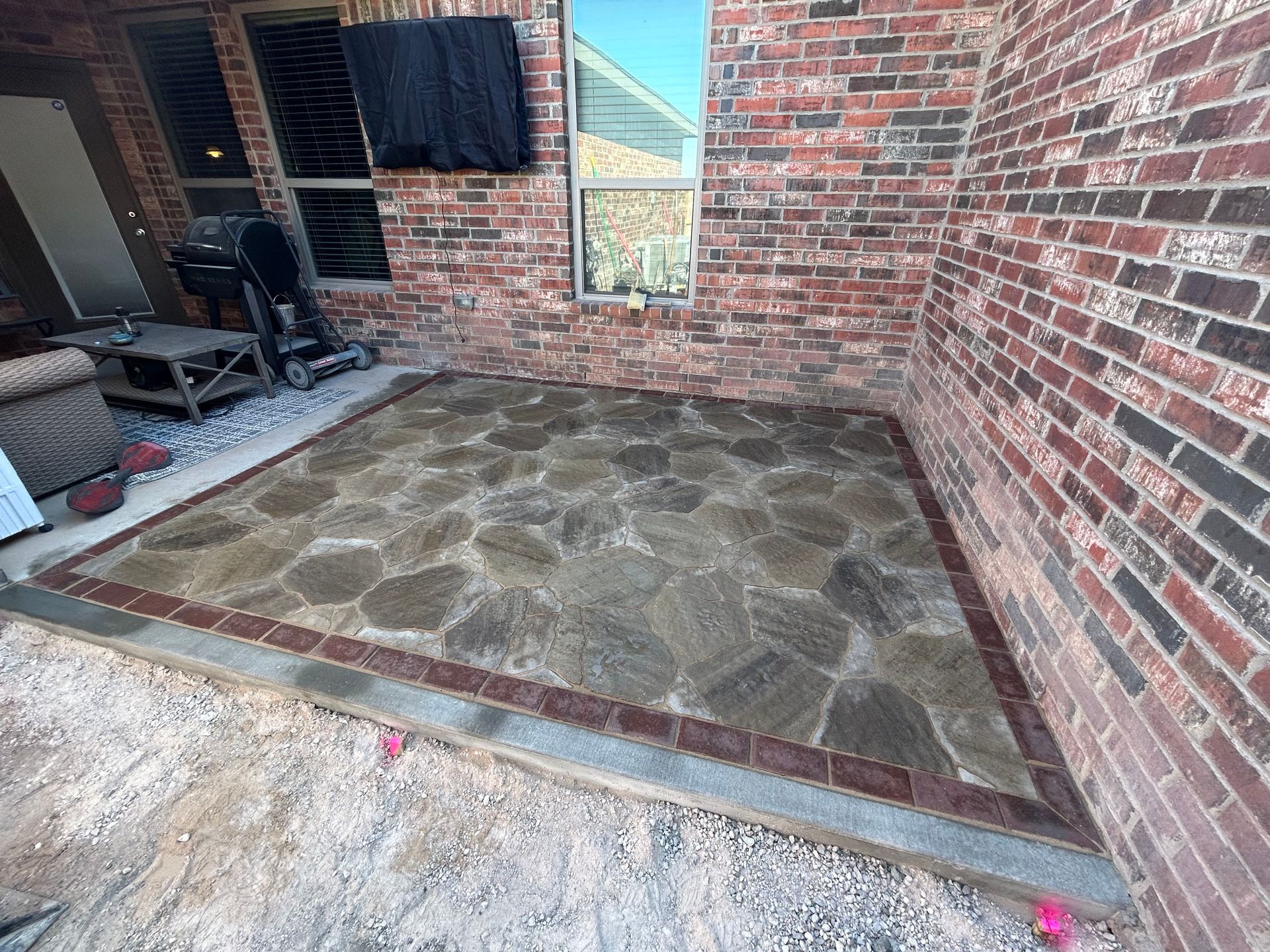 Stone patio beside brick house with patio chairs and a window.