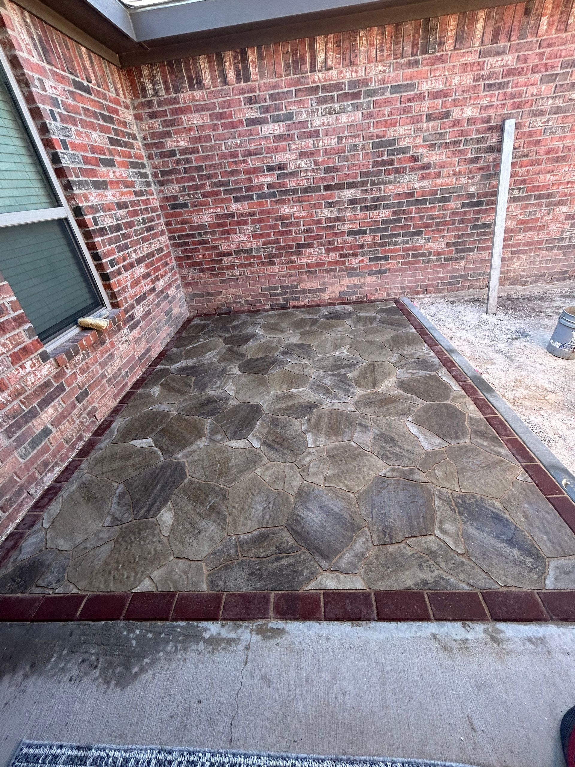 Small stone-paved patio beside a brick wall with a window and white post