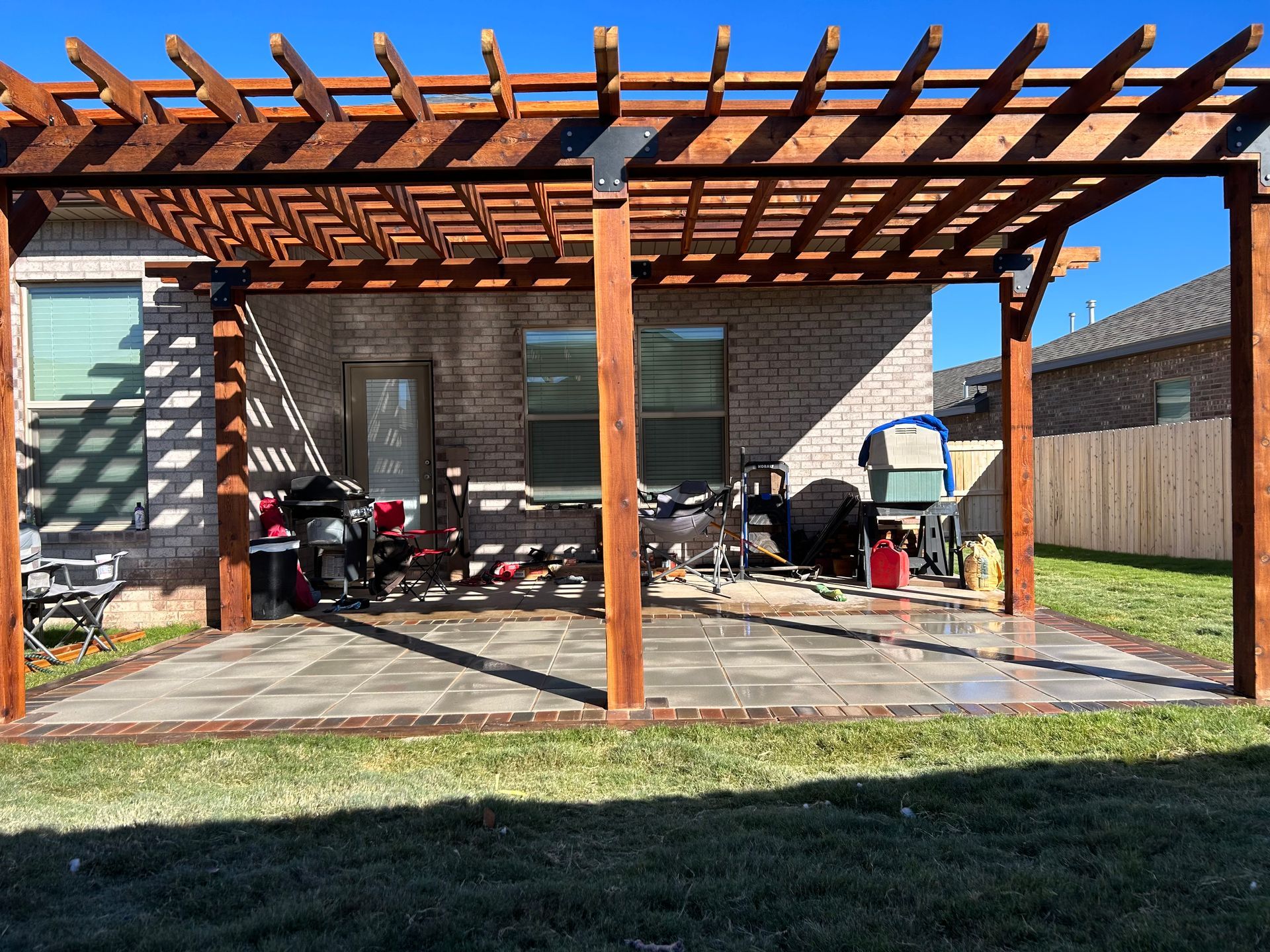 Backyard patio with wooden pergola, brick house wall, and outdoor furniture on a concrete slab.