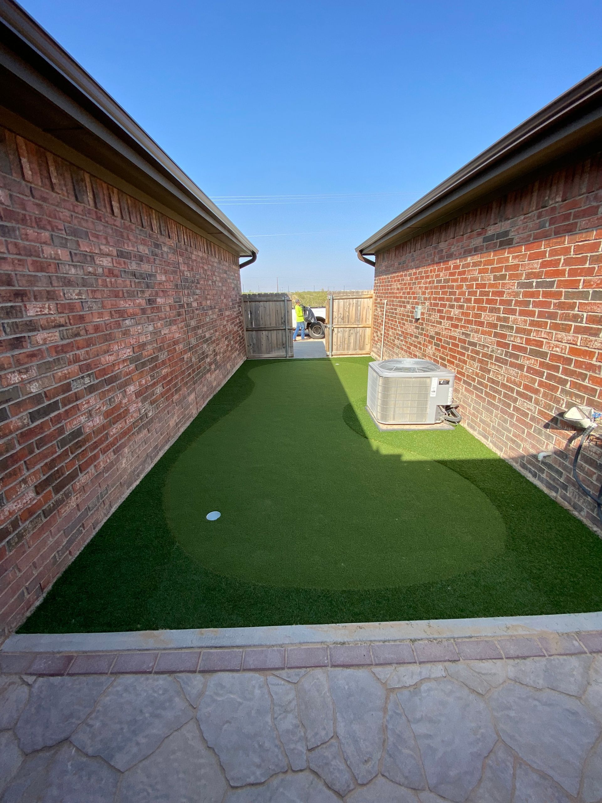 Narrow grass courtyard between two red brick houses, with stone patio in foreground and small AC units on the right