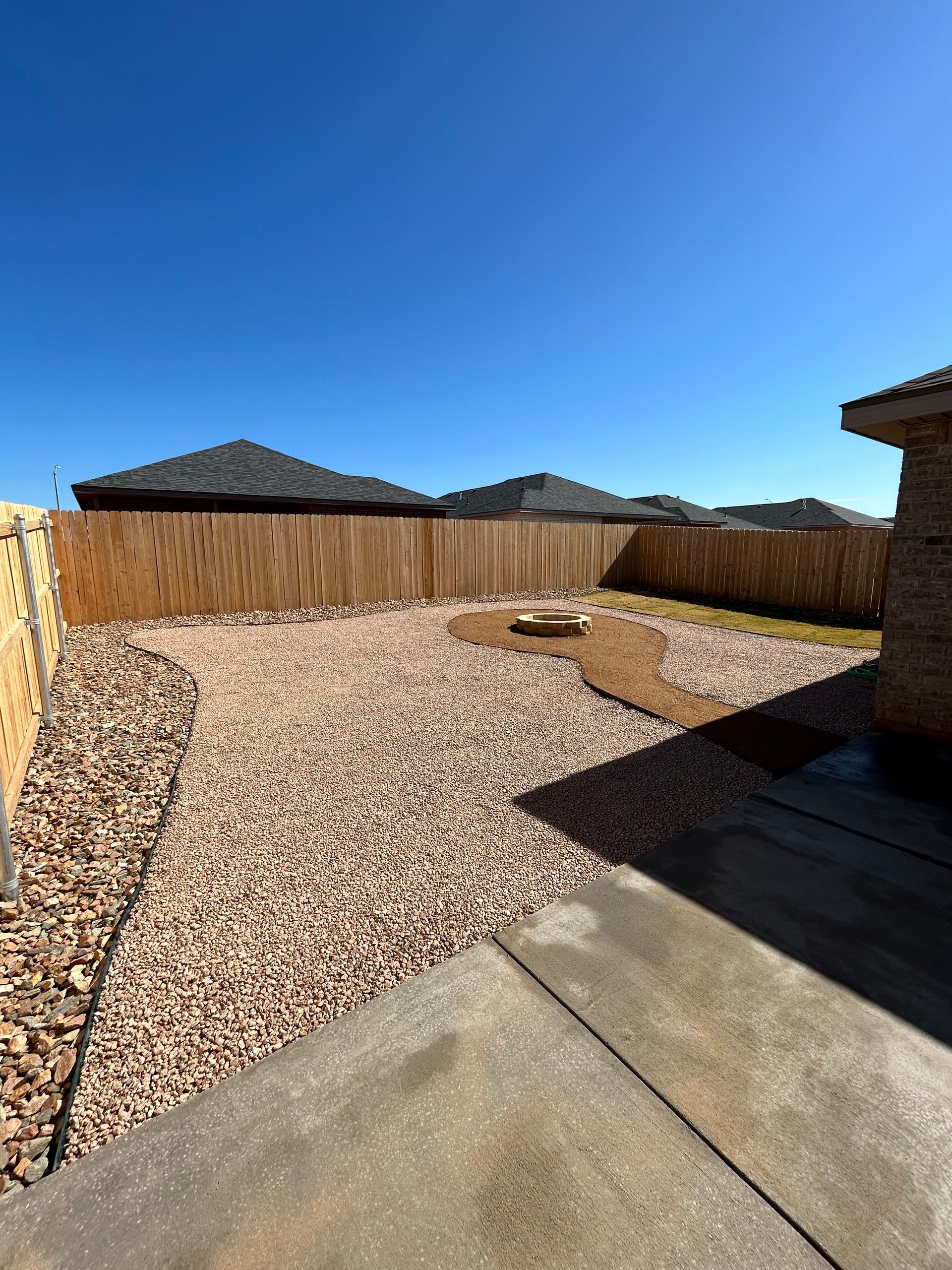 Backyard with gravel ground, concrete patio, wooden fence, and clear blue sky