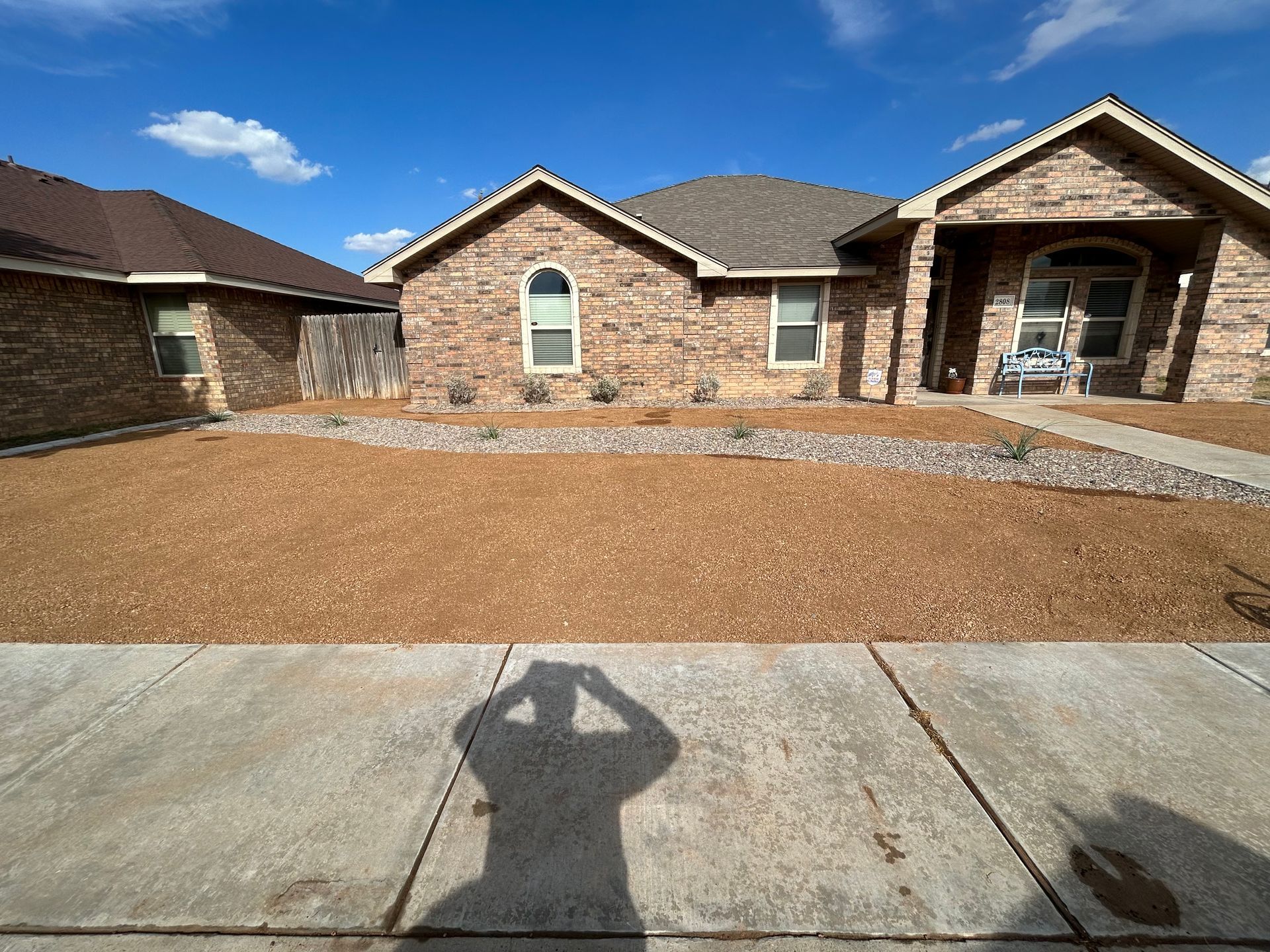Brick house exterior with a gravel front yard and concrete driveway under a blue sky