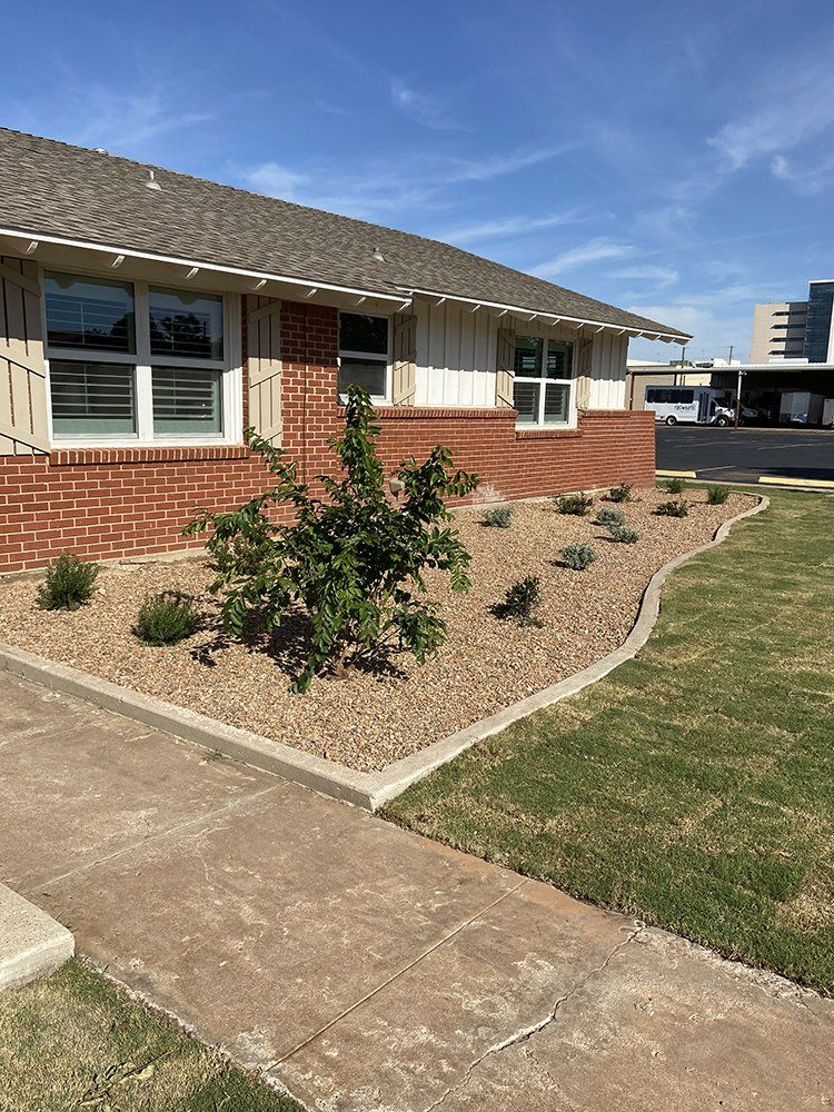 Brick house exterior with windows, concrete walkway, and landscaped front yard under a blue sky