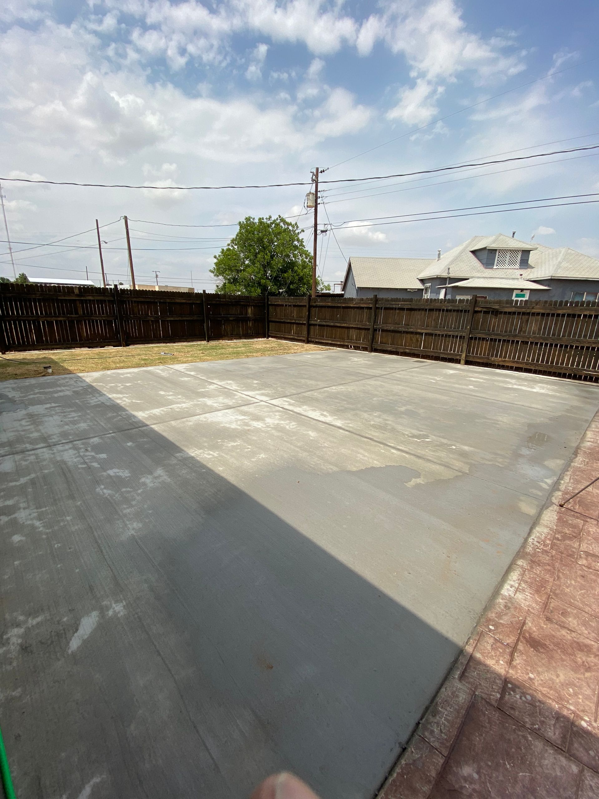 Empty concrete patio with dark fence, string lights, and rooftops under a bright blue sky