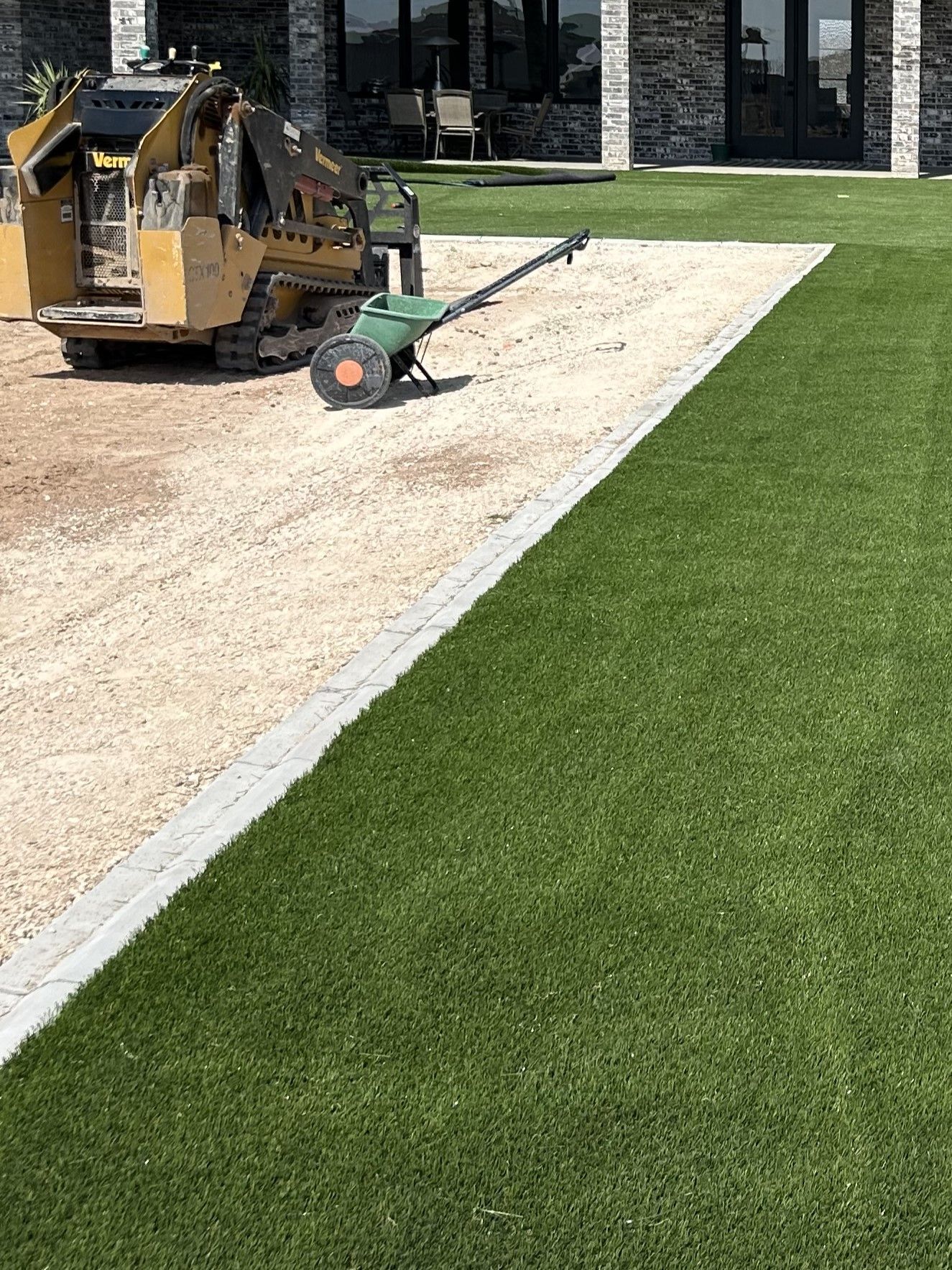 Construction equipment leveling a gravel path beside a green lawn and building.
