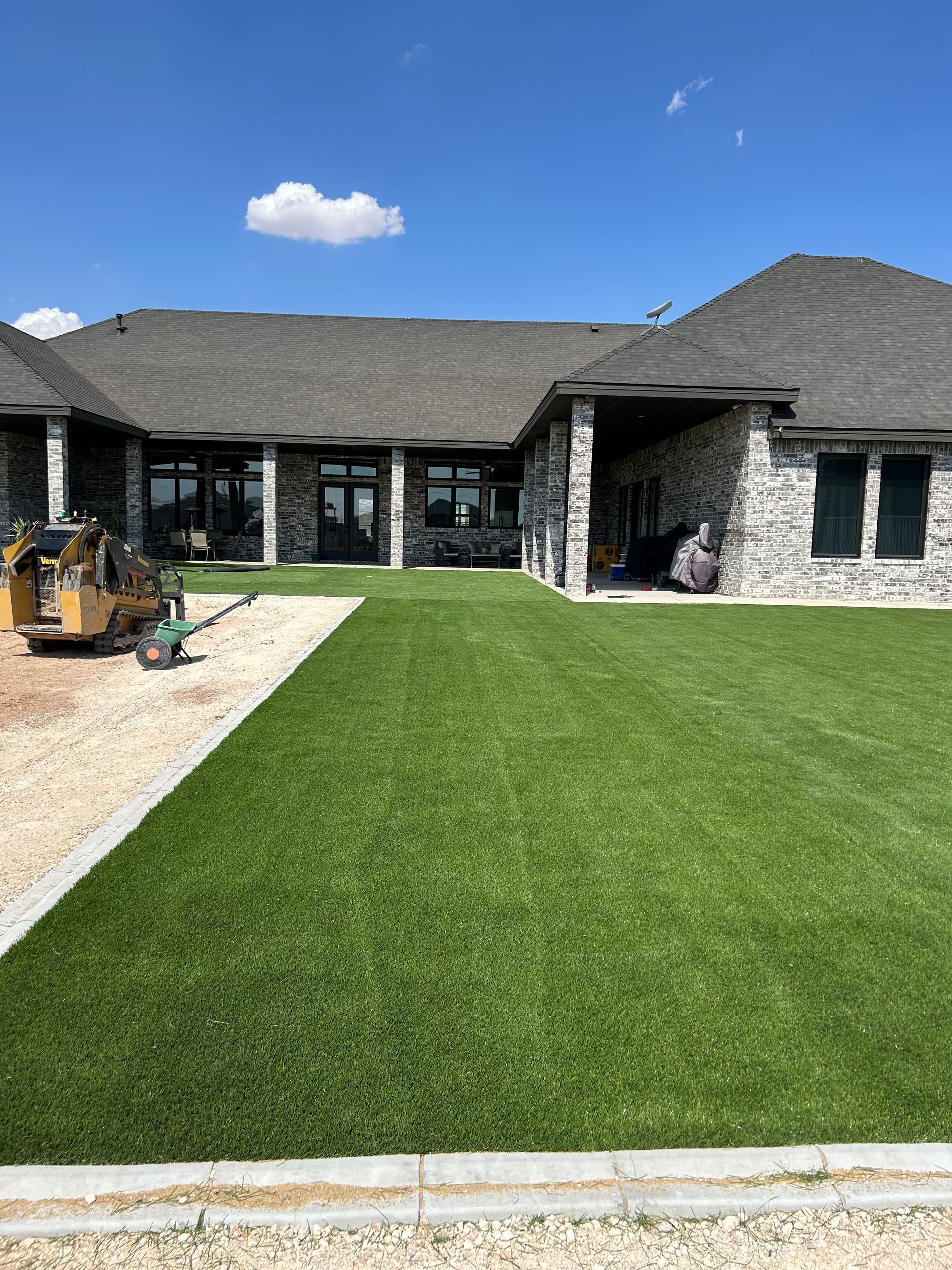 Modern house exterior with a large green lawn, stone facade, and blue sky