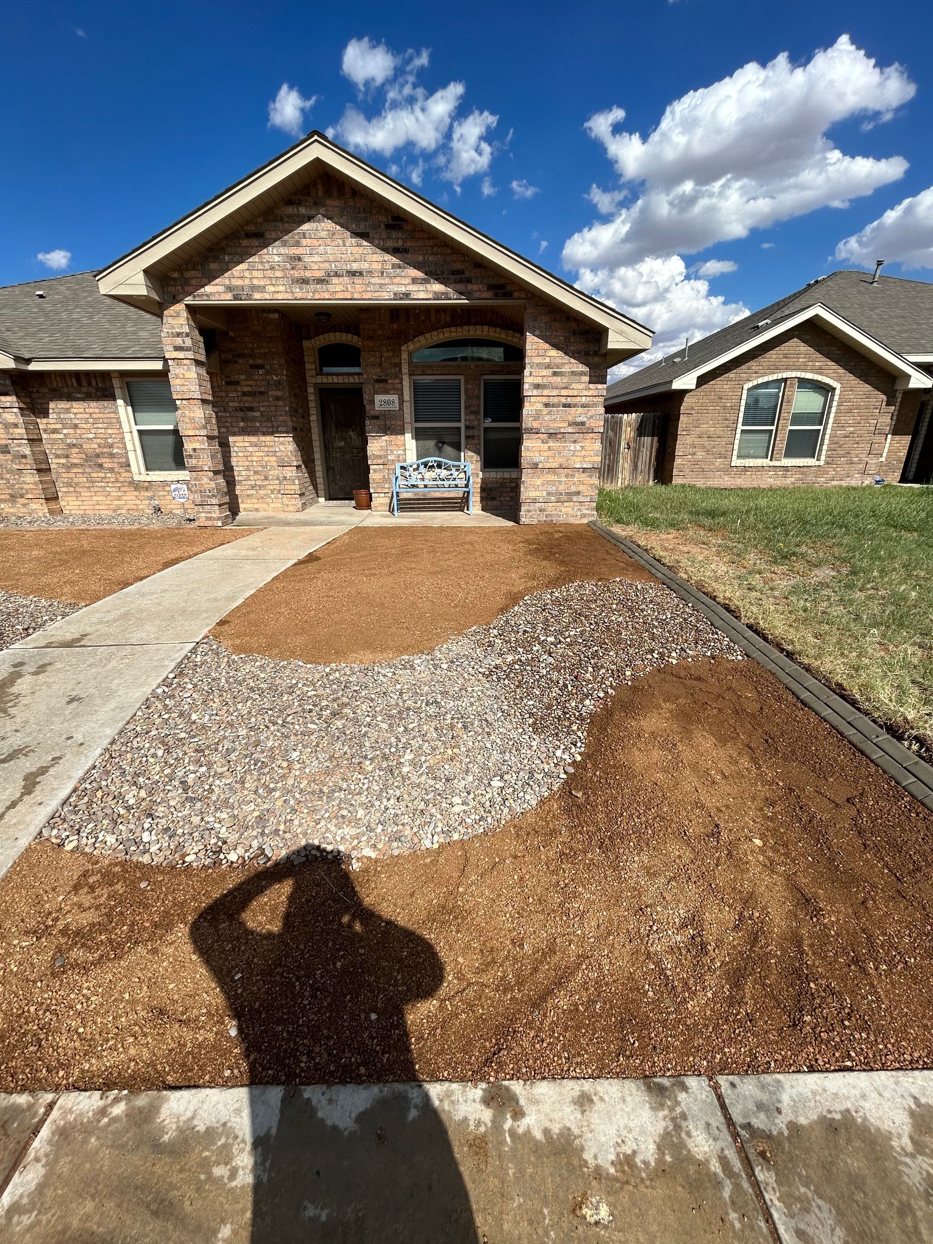 Brick house with a concrete walkway and fresh gravel landscaping under a blue sky.