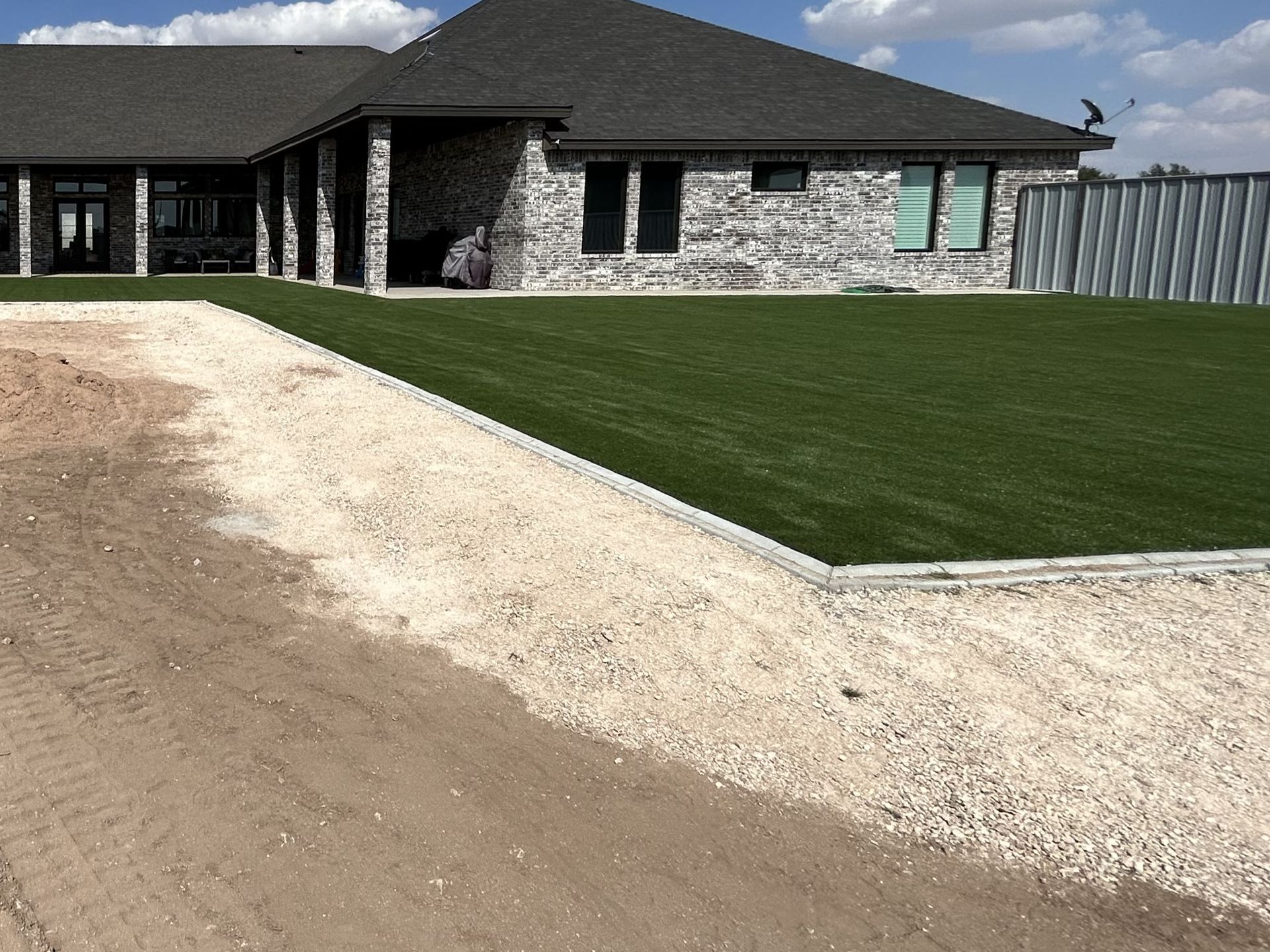 Modern brick house with dark roof, green lawn, and gravel driveway under a cloudy sky