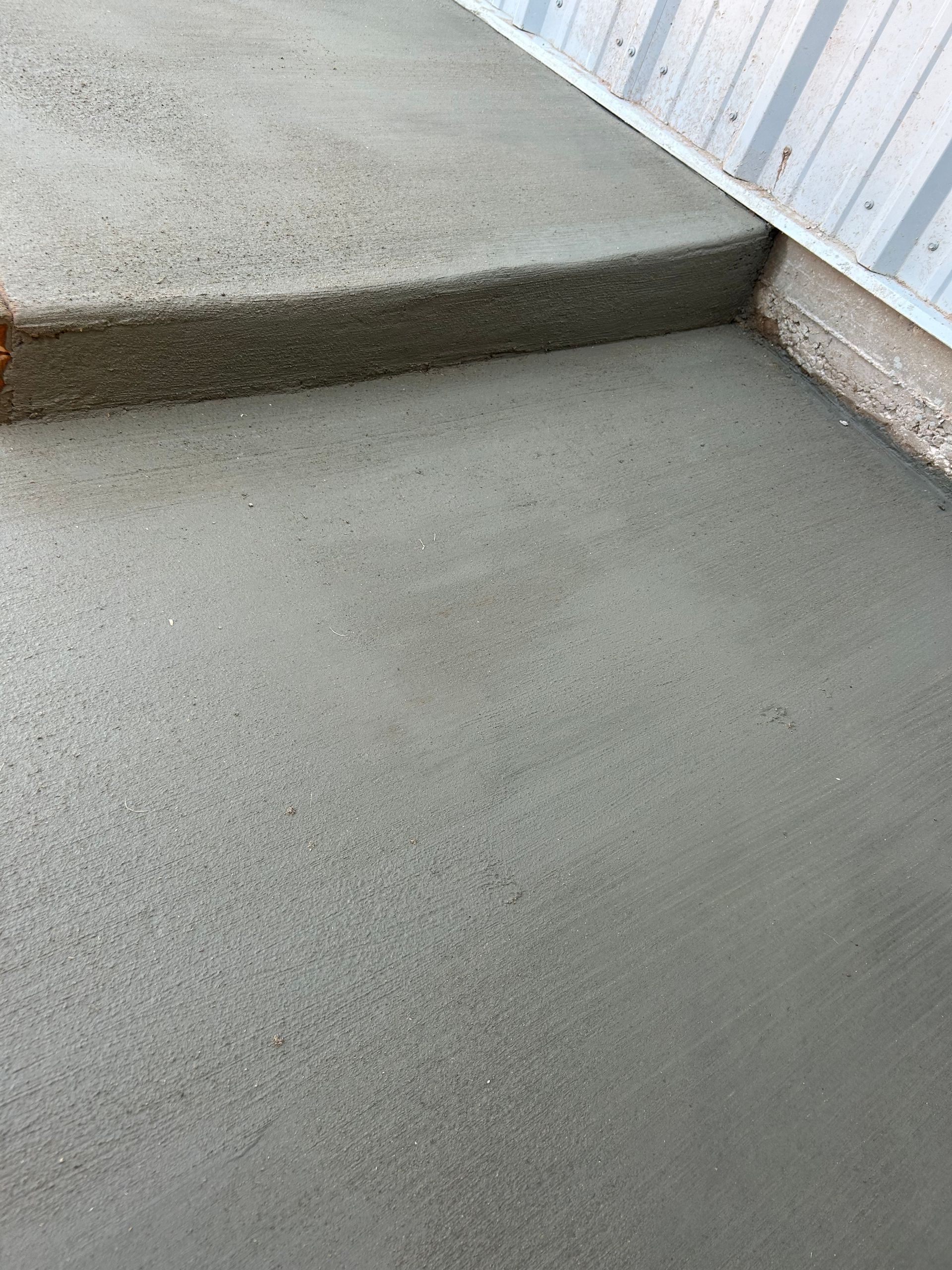 Concrete step and landing beside a white corrugated wall and railing