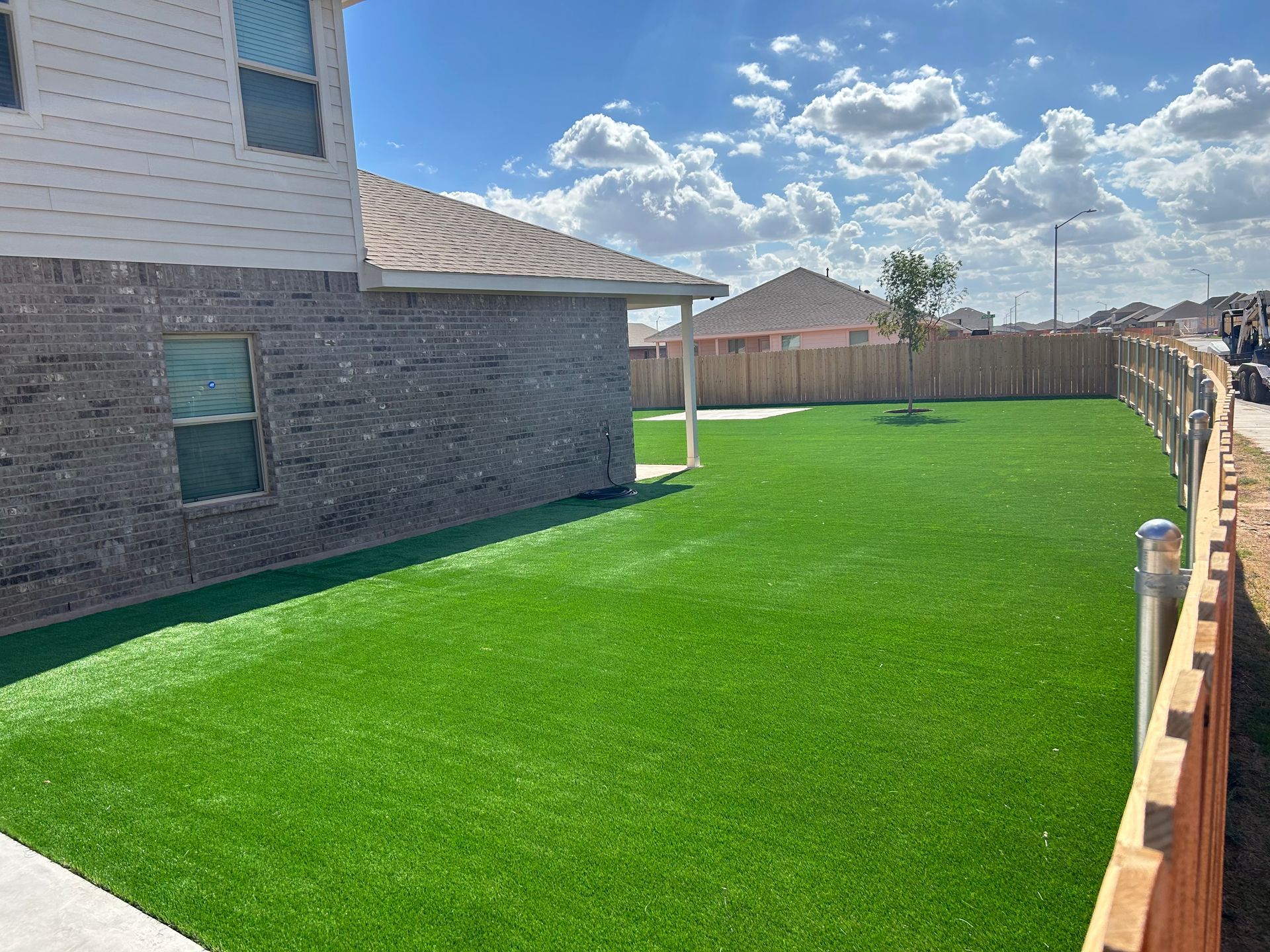 Backyard with bright green lawn, brick house, wooden fence, and cloudy sky