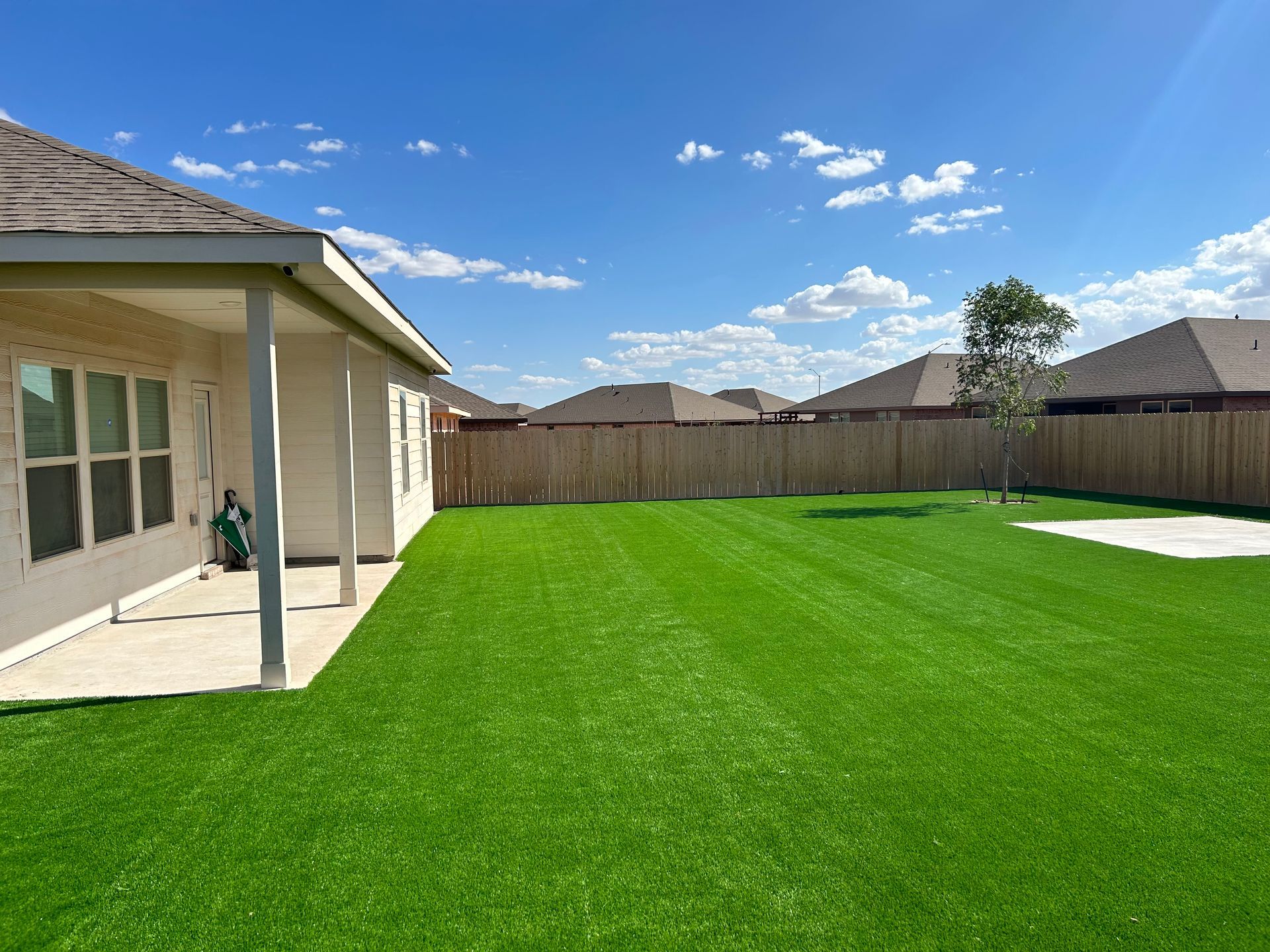 Backyard with bright green lawn, covered patio, wooden fence, and clear blue sky