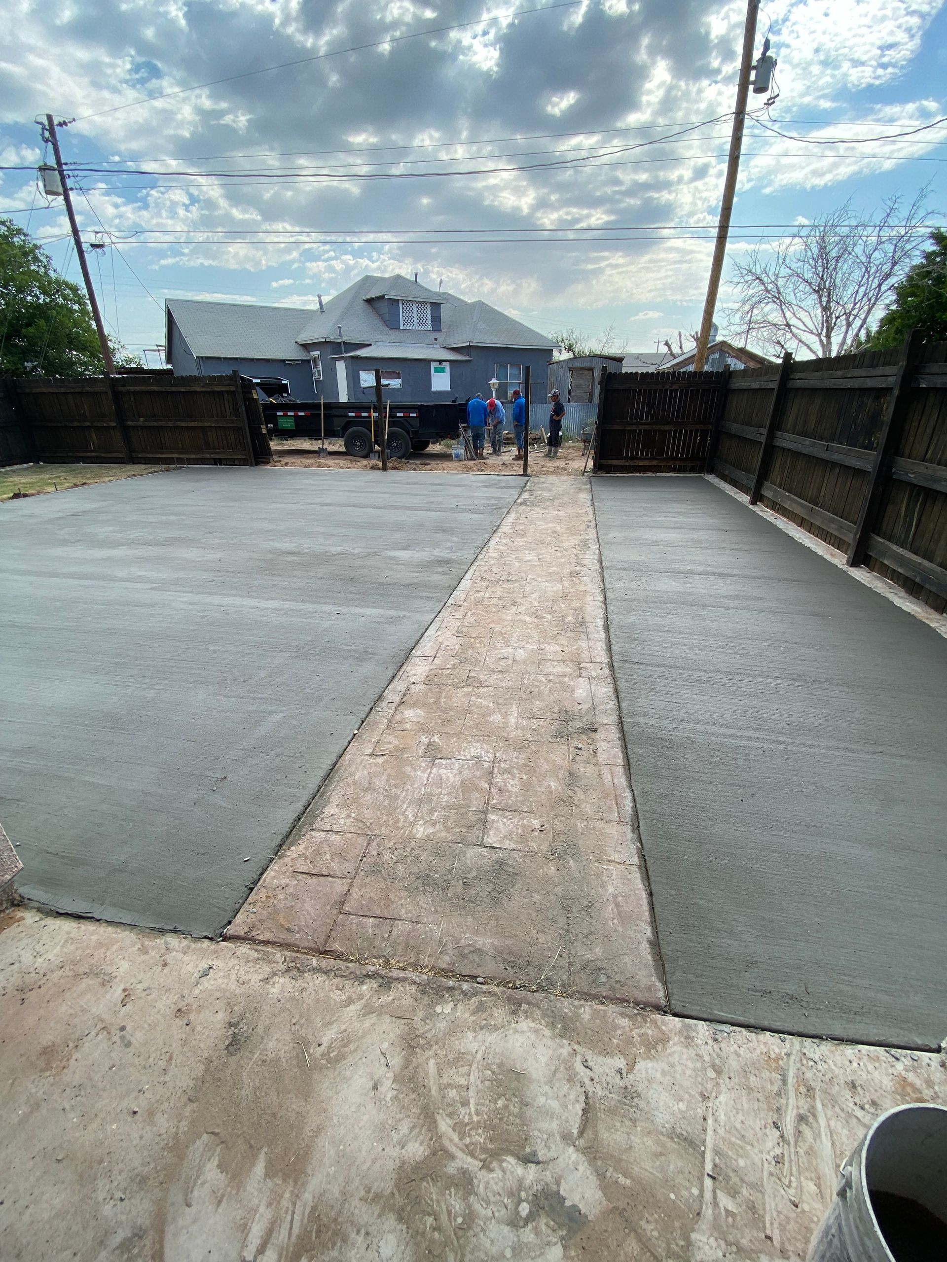 Wide driveway leading to a house, with a central gravel strip, black fences, and people near the entrance.
