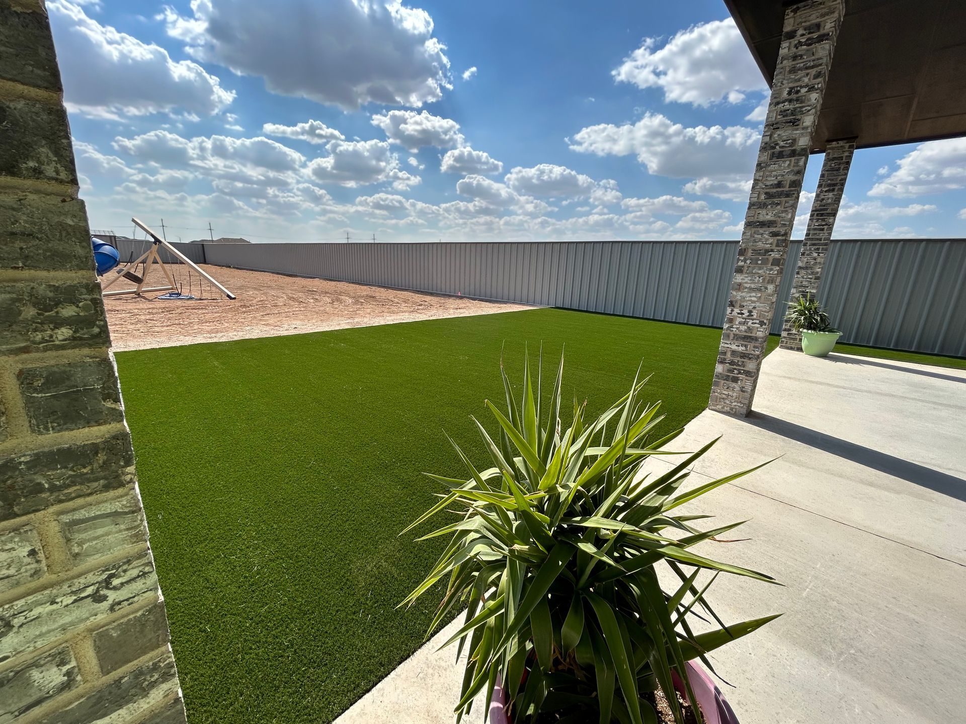 Backyard patio overlooking a newly sodded green lawn and fenced yard under a cloudy blue sky