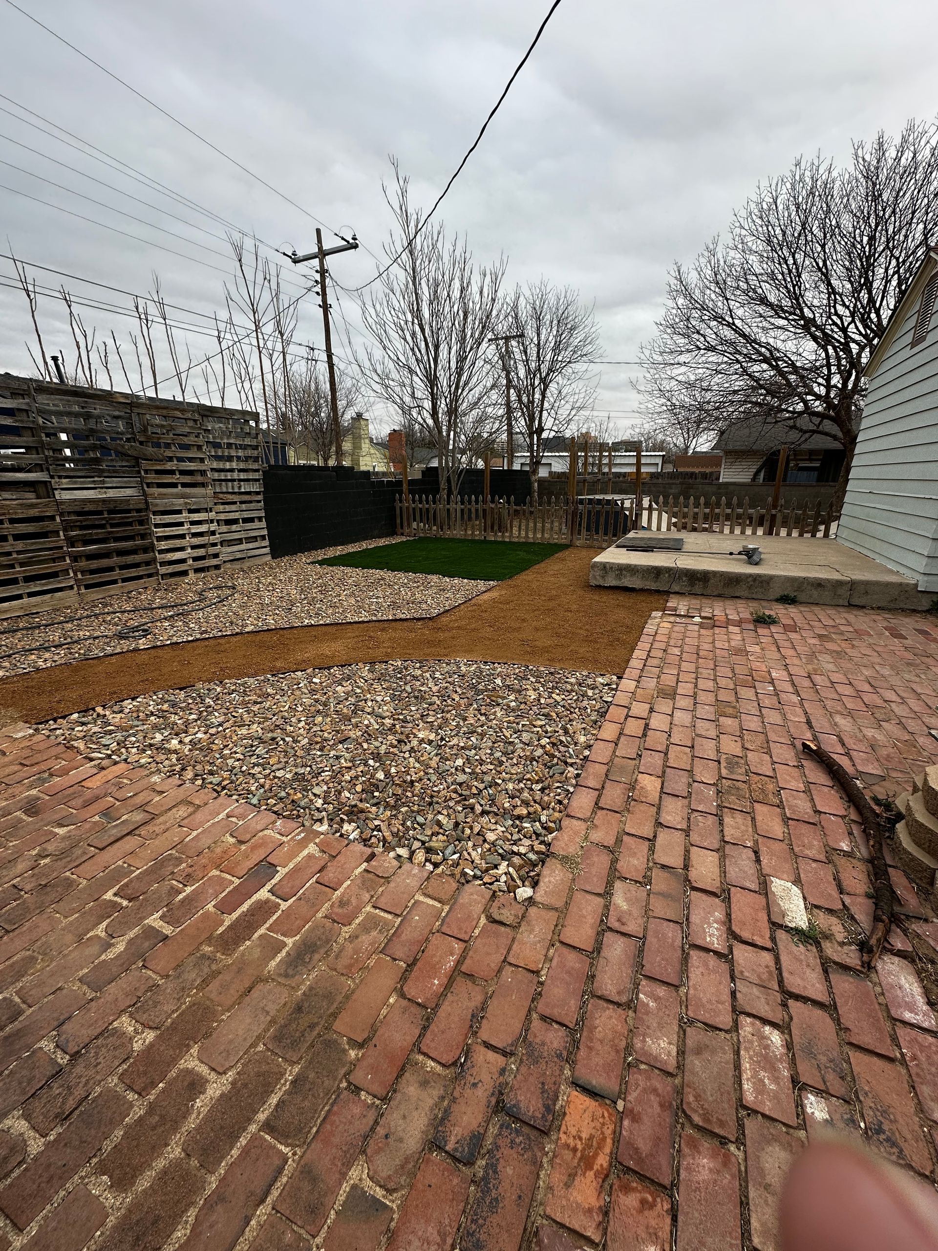 Brick patio and gravel backyard with leafless trees and overcast sky