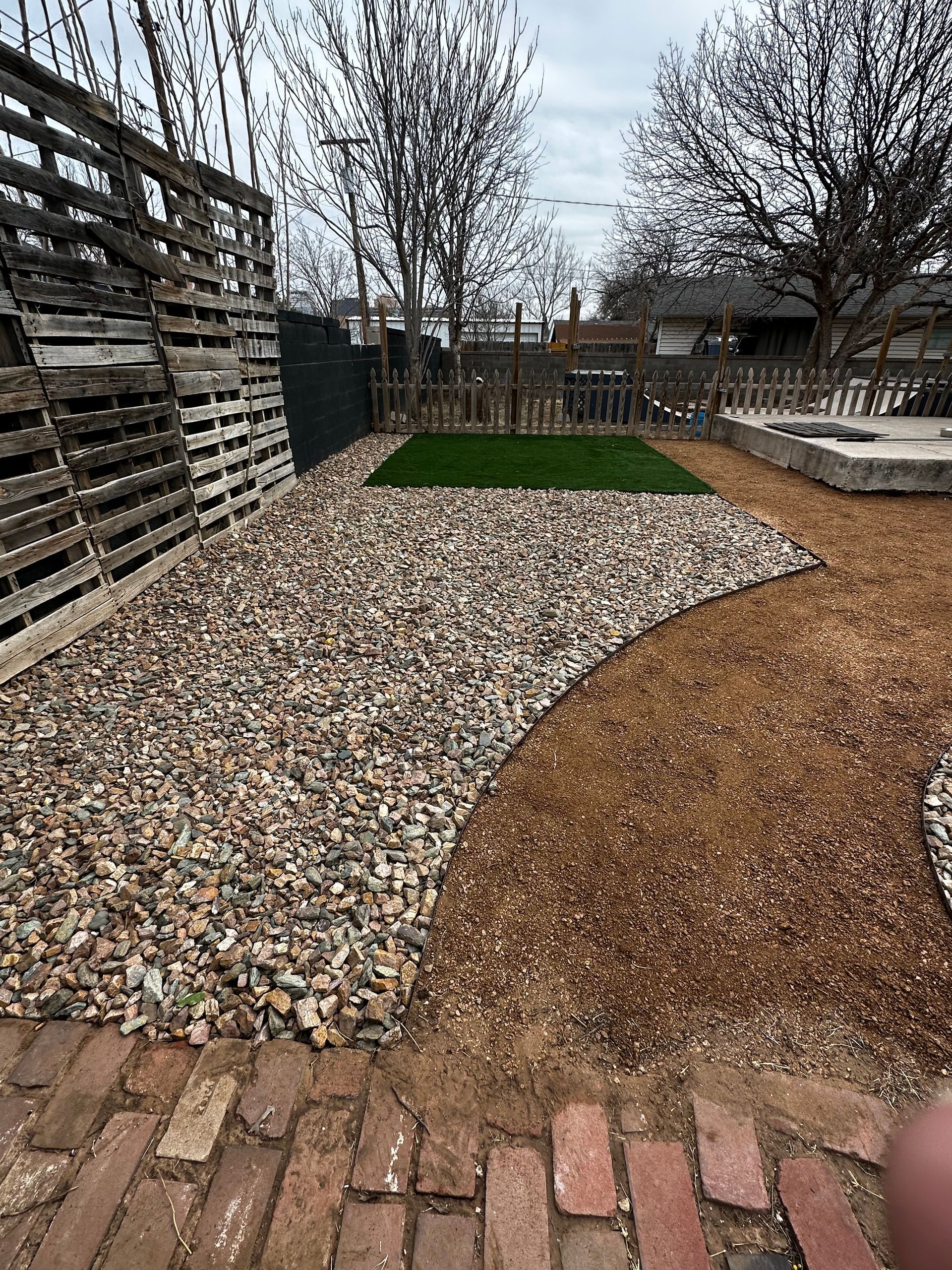 Backyard garden with gravel paths, brick edging, a small grass patch, and bare trees
