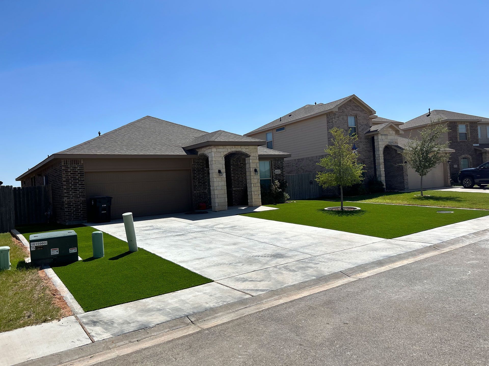 Suburban house with a concrete driveway, green lawn, and trash bins by the curb under a clear blue sky