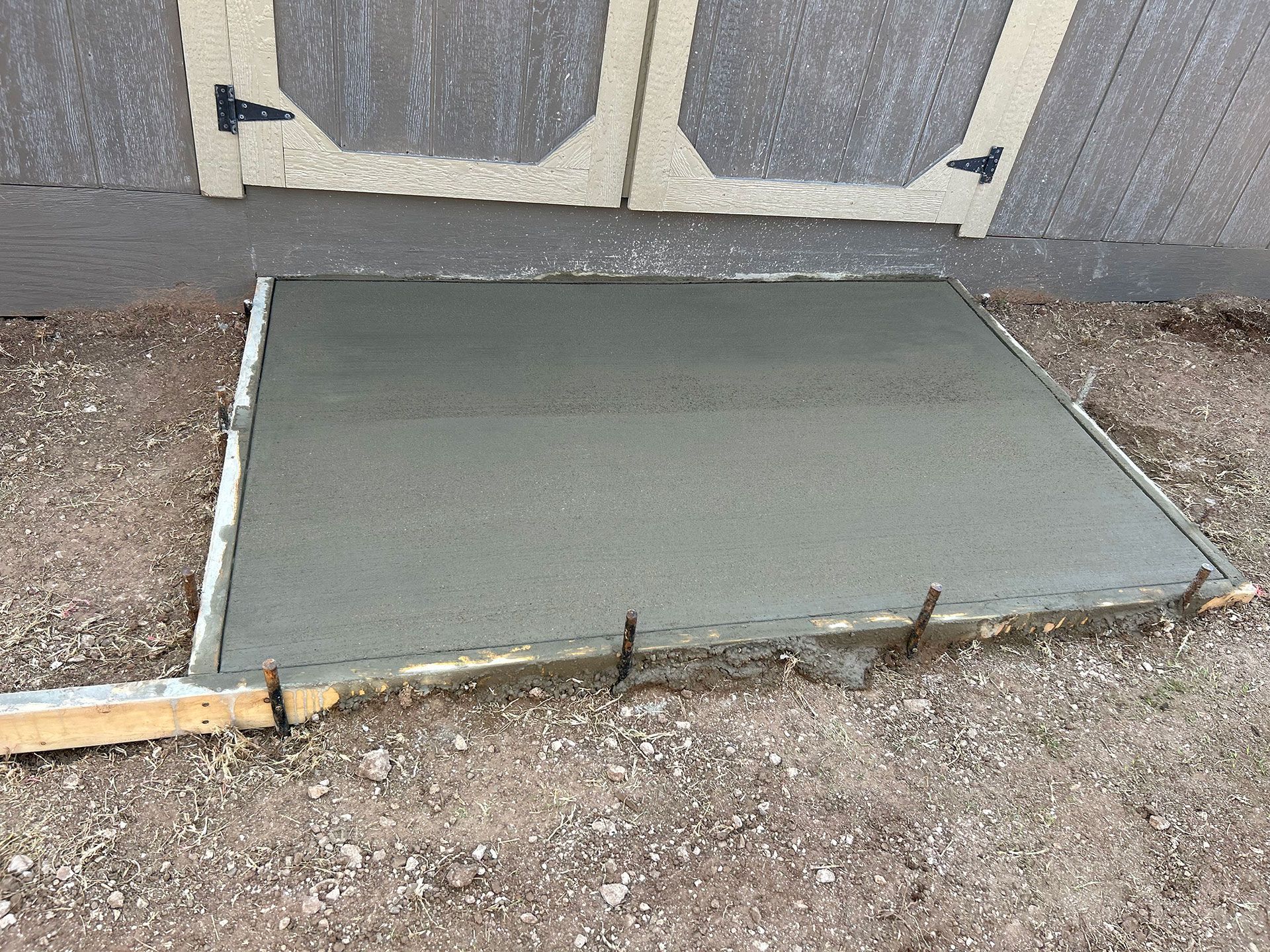 Freshly poured concrete ramp or pad in front of a door, bordered by gravel.