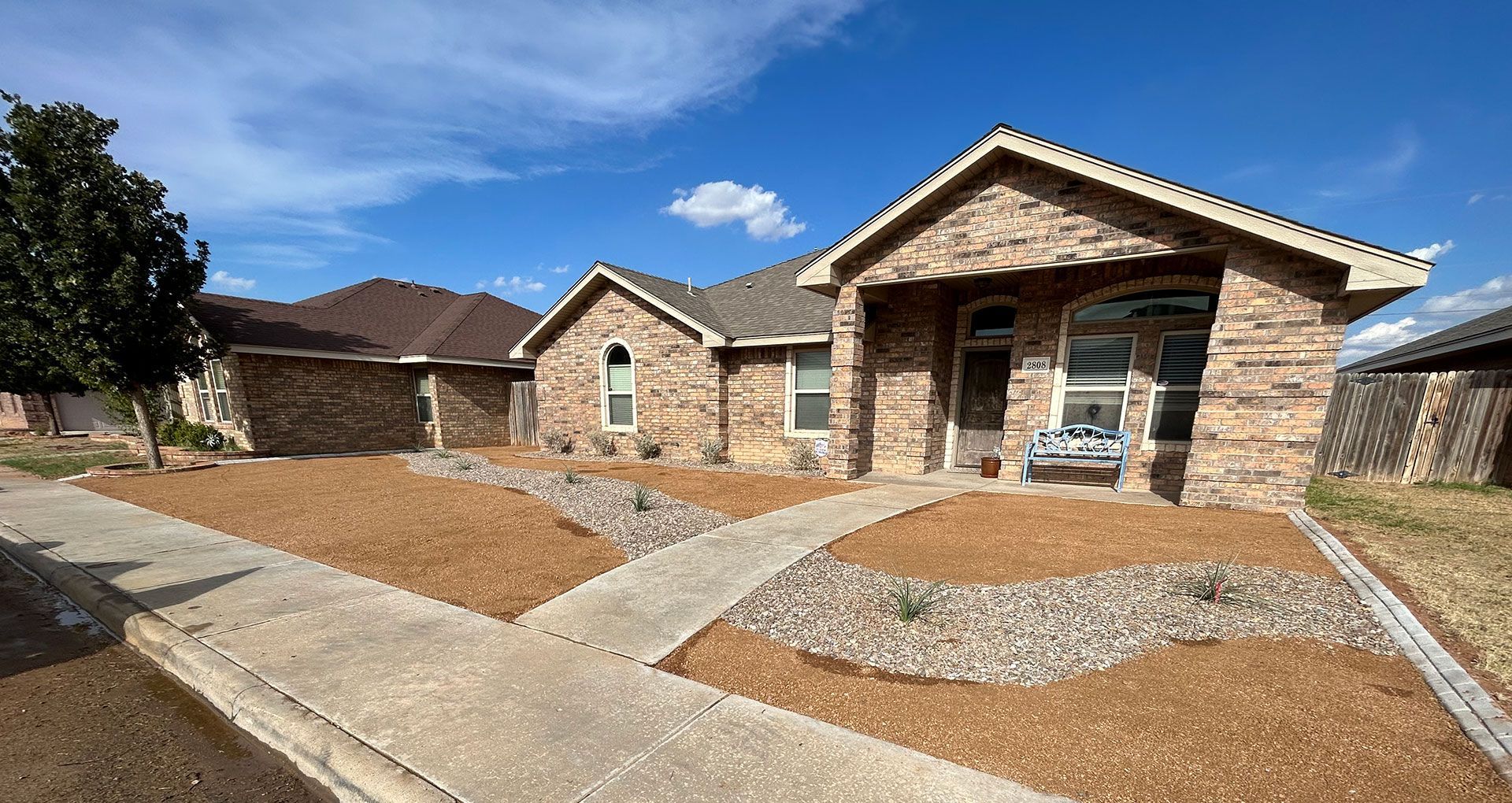 Brick suburban house with a landscaped front yard, curved stone walkway, and clear blue sky