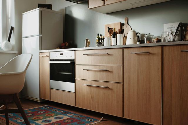 Kitchen with wooden cabinets, stainless steel oven, refrigerator, and colorful rug.